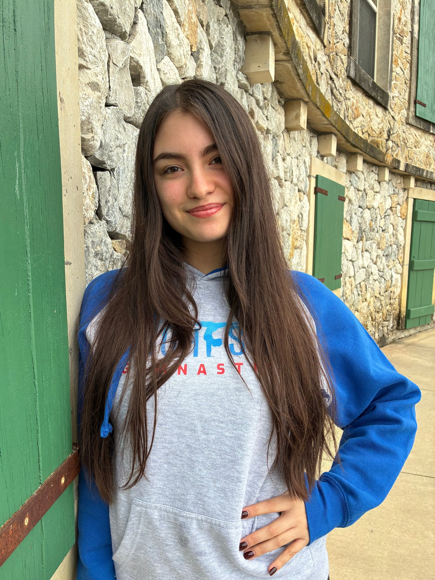 A man wearing a grey t-shirt is standing in front of a stone wall.