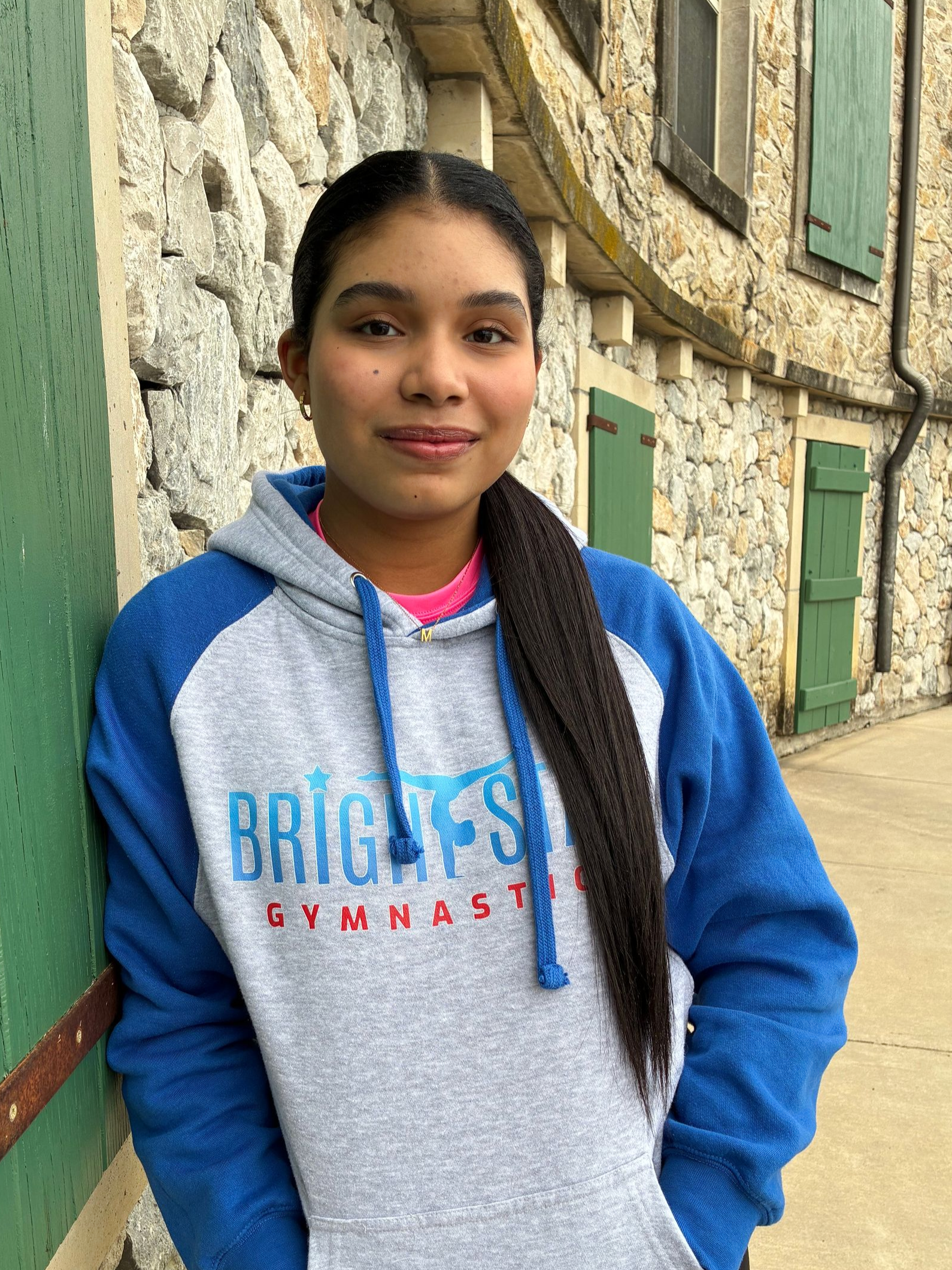 A man wearing a grey t-shirt is standing in front of a stone wall.
