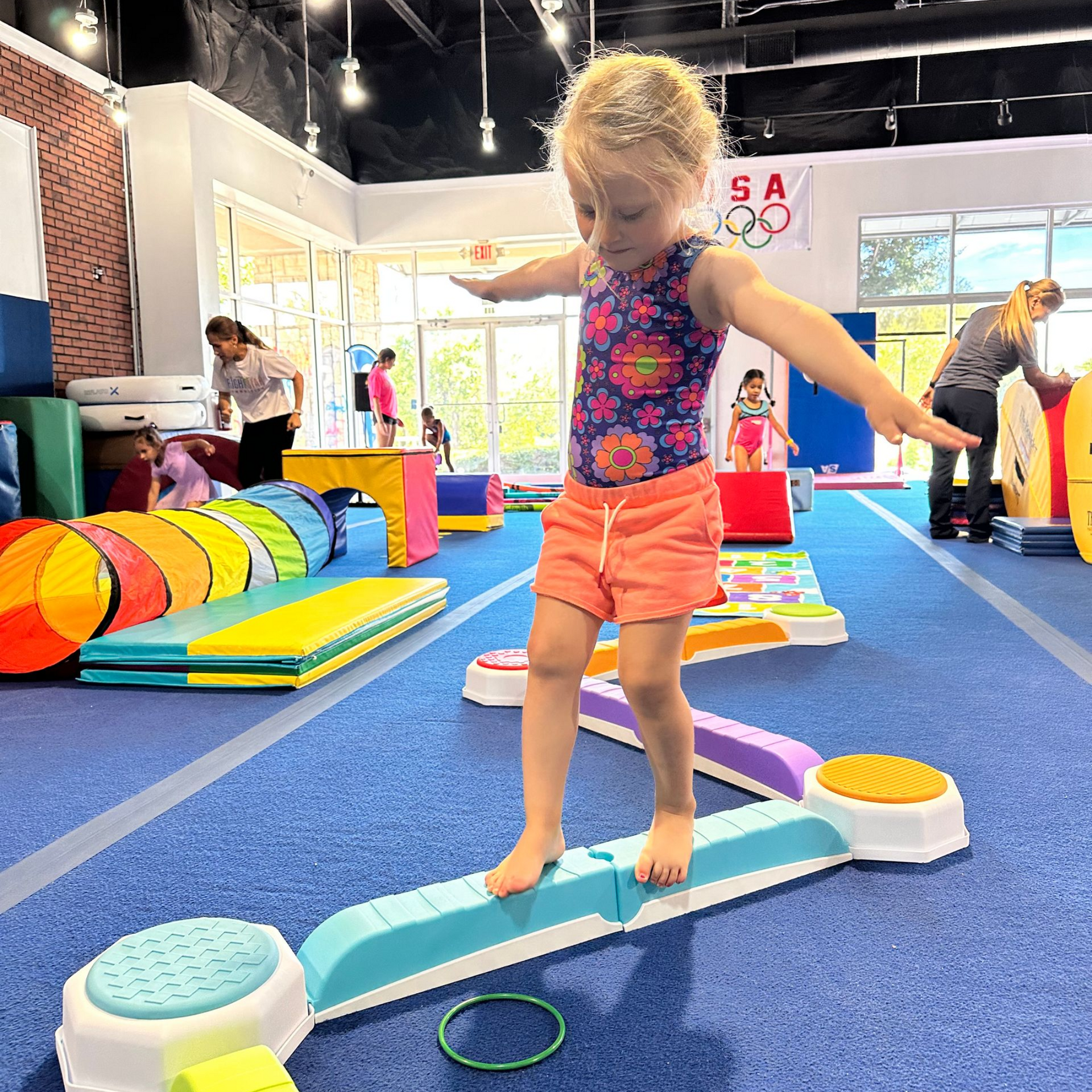 A baby in a striped tank top is hanging from gymnastic rings