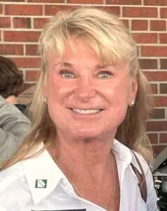 A woman in a white shirt is smiling in front of a brick wall.