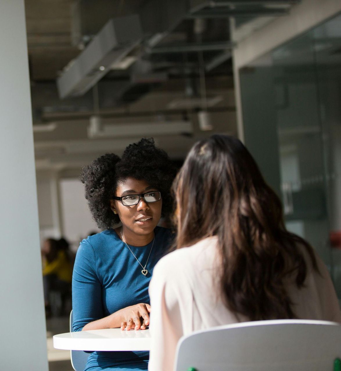 Two women are sitting at a table talking to each other