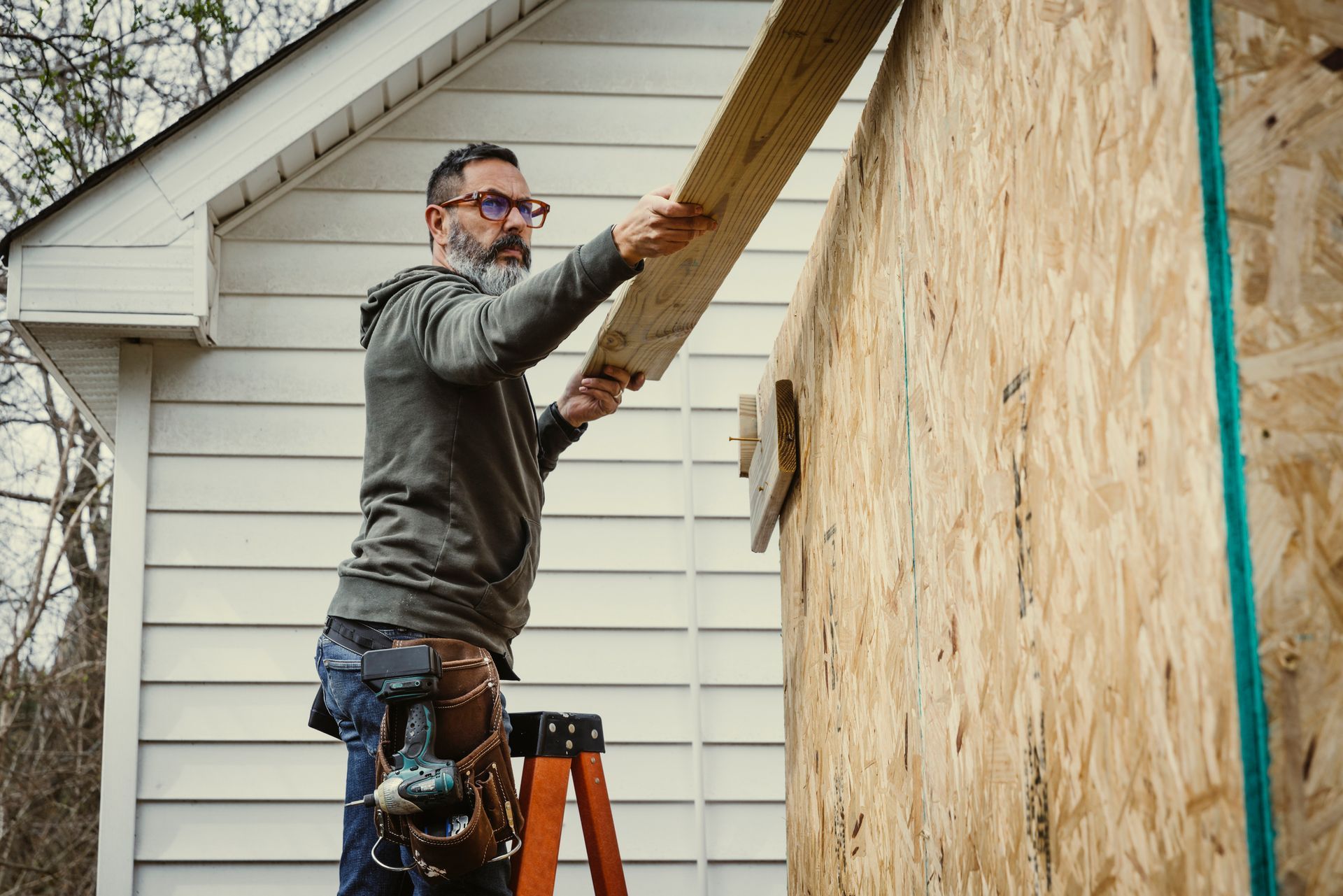 Person installing a wooden plank on an exterior wall using a ladder.