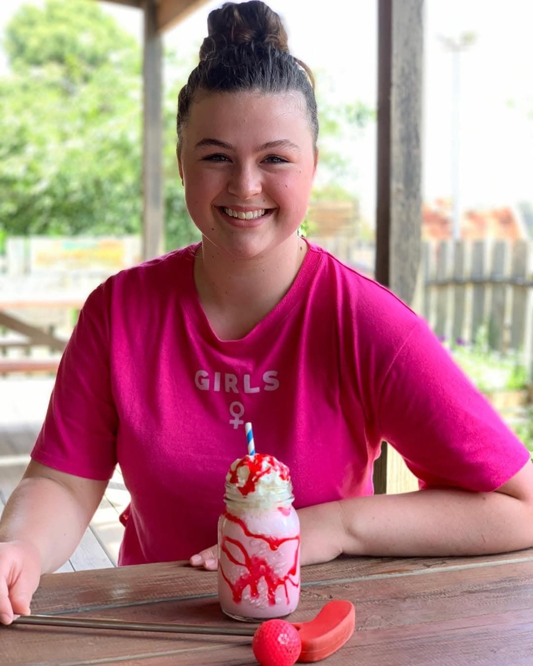 A Girl in a Pink Shirt is Sitting at a Table With a Milkshake on It — Gold Rush Mini Golf in Warrenheip, VIC