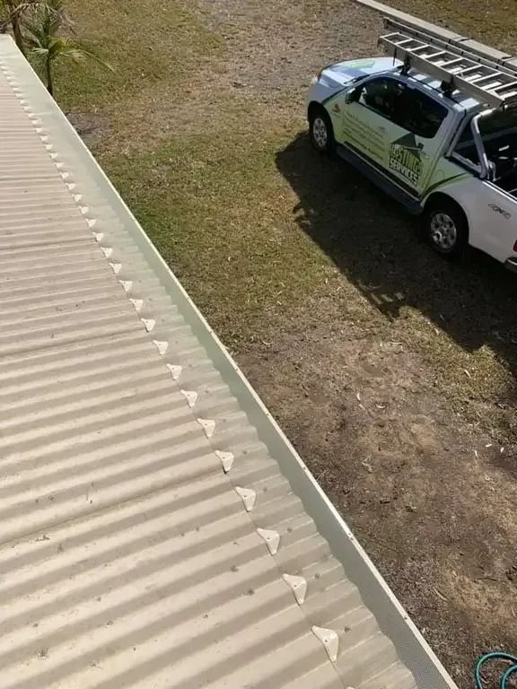 White corrugated roof with attached plastic rain deflectors; a white pickup truck is parked nearby on the grass.— Gutter Guard In Lake Cathie, NSW