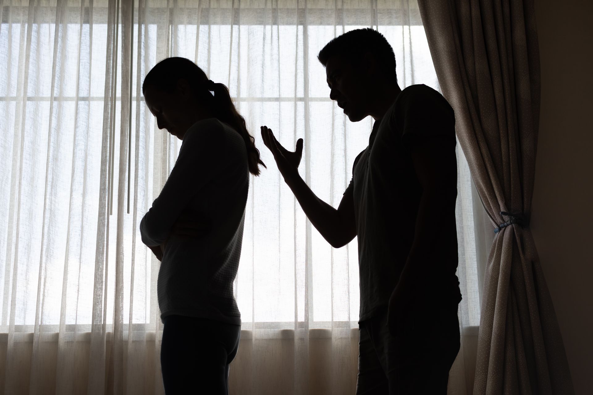 Two silhouetted people arguing in front of a window with curtains Two silhouetted people arguing in front of a window with curtains