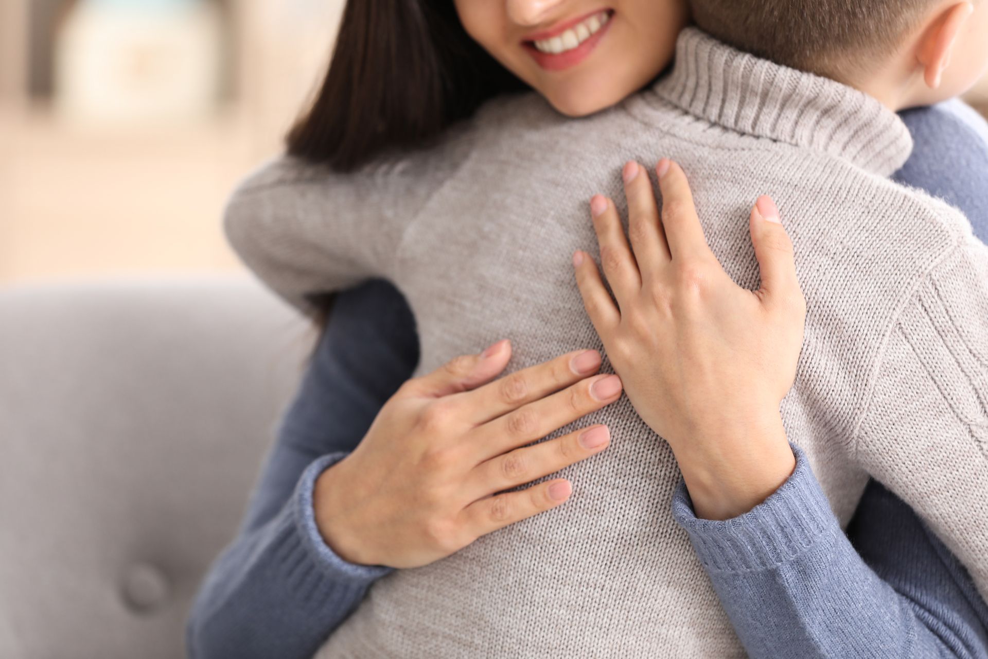 Two people hugging on a couch, with one wearing a gray sweater and the other a blue sweater.