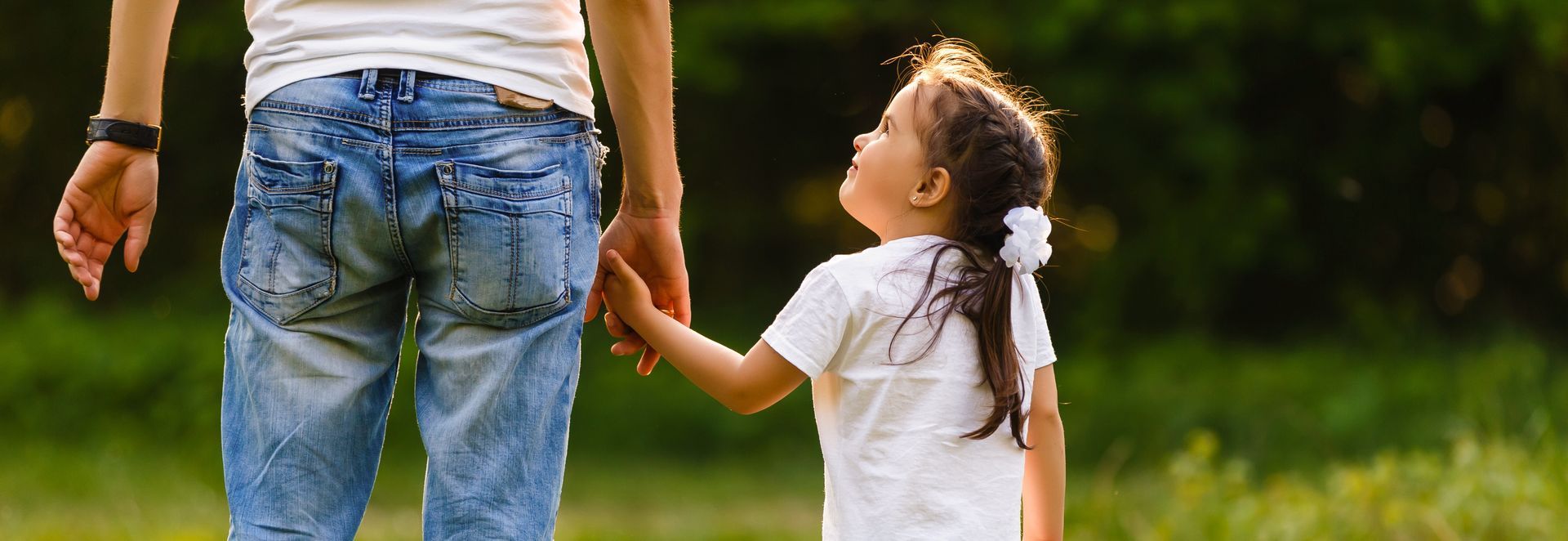 Adult holding hands with a child walking outdoors on a grassy path