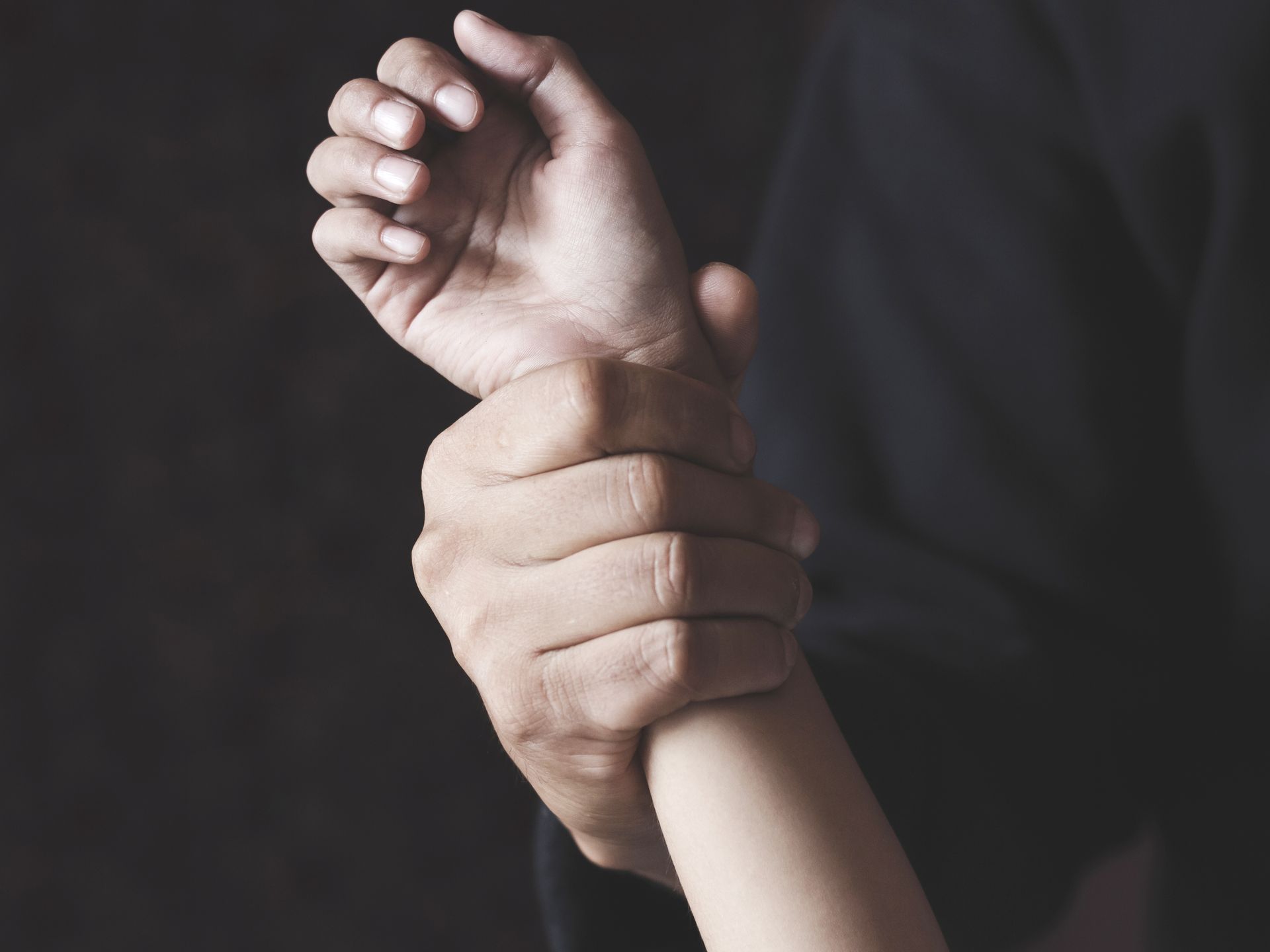 Hand gripping a smaller wrist against a dark background Hand gripping a smaller wrist against a dark background