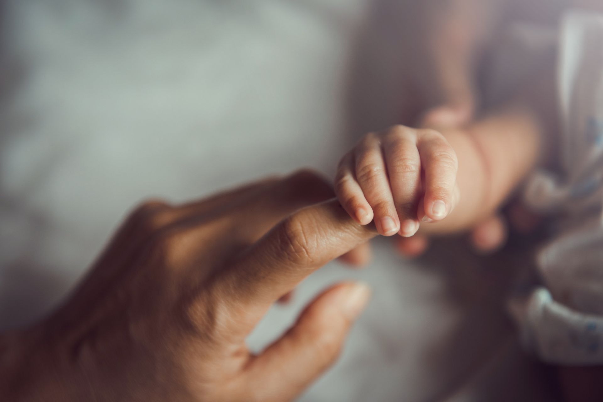 Adult hand gently holding a baby’s tiny fingers in a soft, warm close-up