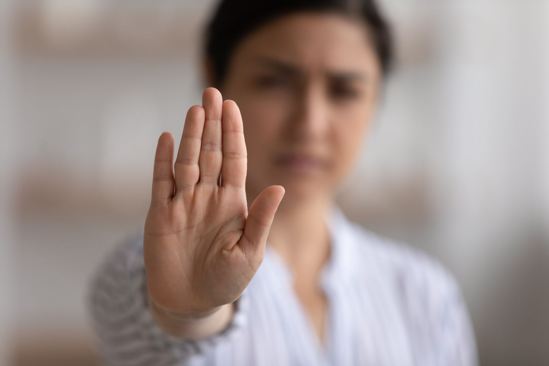 Person holding up a palm in a stop gesture, blurred background indoors Person holding up a palm in a stop gesture, blurred background indoors