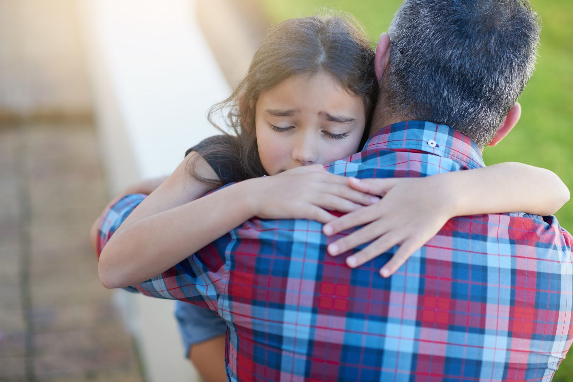 Two people hugging outdoors, one with a plaid shirt comforting the other with eyes closed