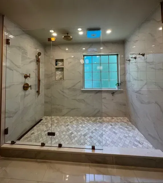Spacious shower with marble-like tile walls and mosaic floor. Glass door and window, bronze fixtures.