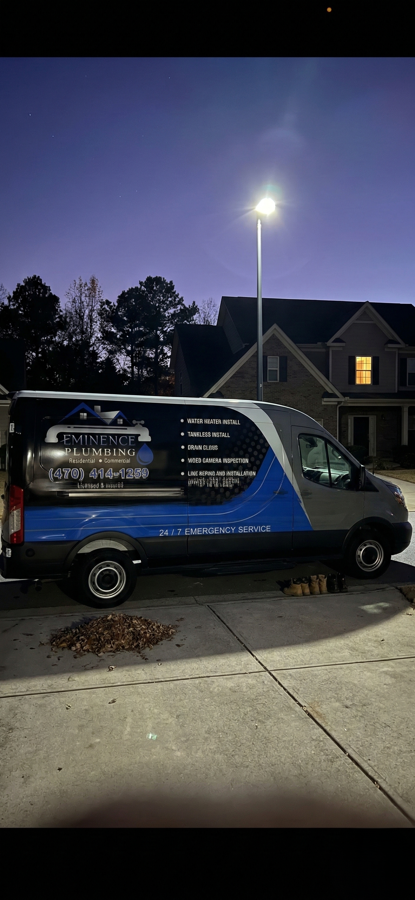 Van parked on pavement with service logo, nighttime setting, streetlight, house in background.