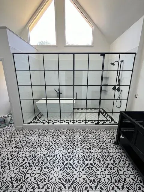 Spacious bathroom with black framed shower, tub, and black and white patterned floor tiles. Windows in the high ceiling.