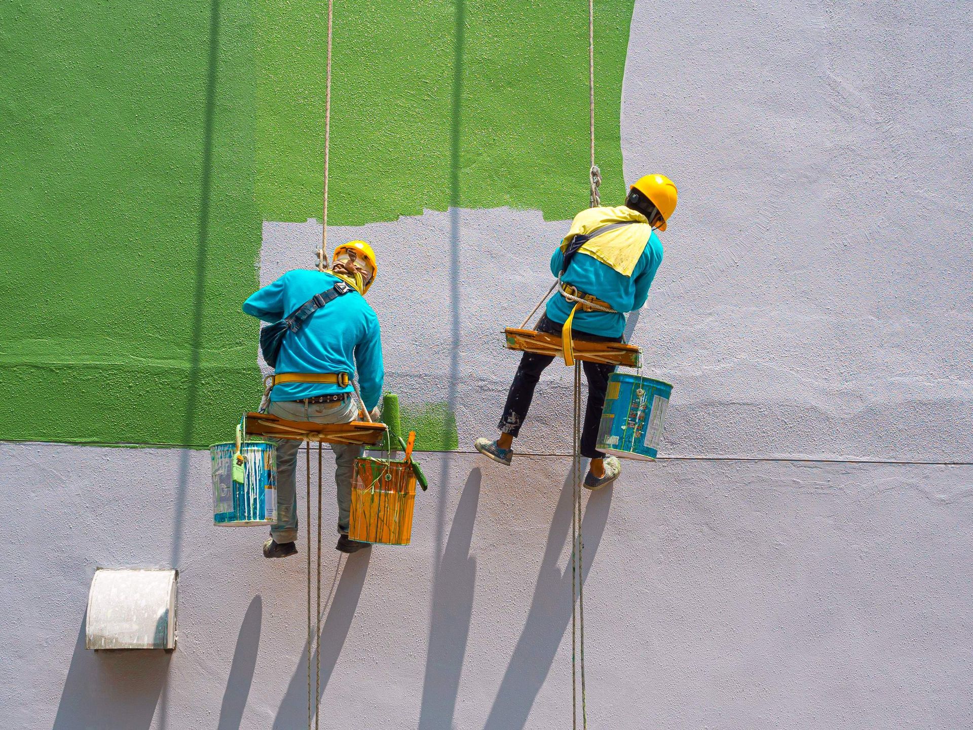 Two men are painting a wall on a rope