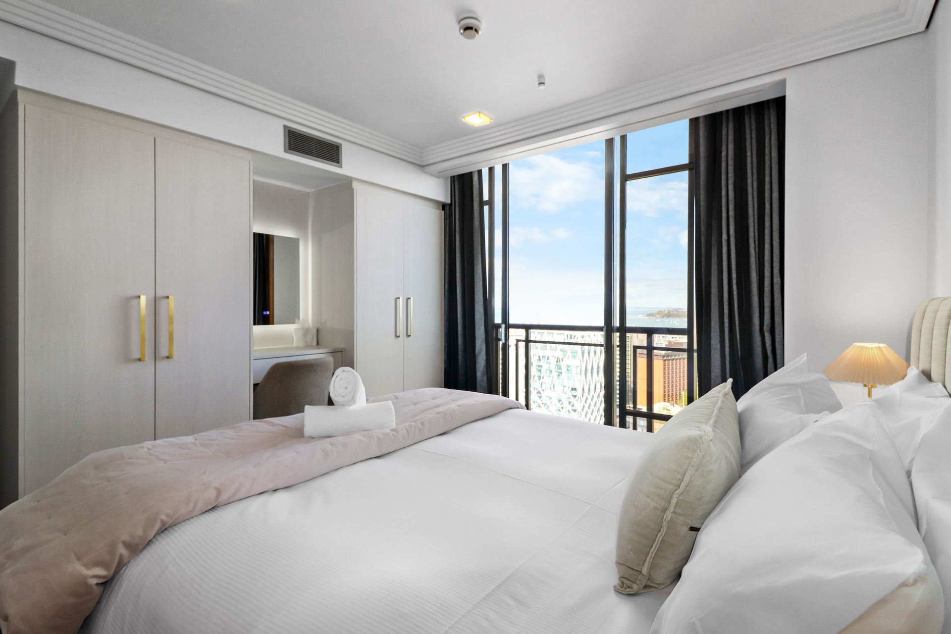 Spacious white living room with curved windows overlooking city and water view; marble table with flowers.