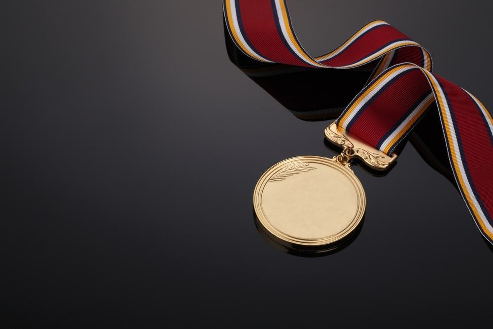 Gold Medal With A Red Ribbon On A Black Surface — Accolades Awards Hunter Valley In Maitland, NSW