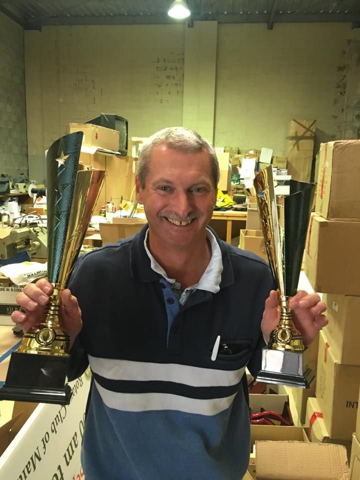 Man Holding Up Two Trophies In A Warehouse — Accolades Awards In Maitland, NSW