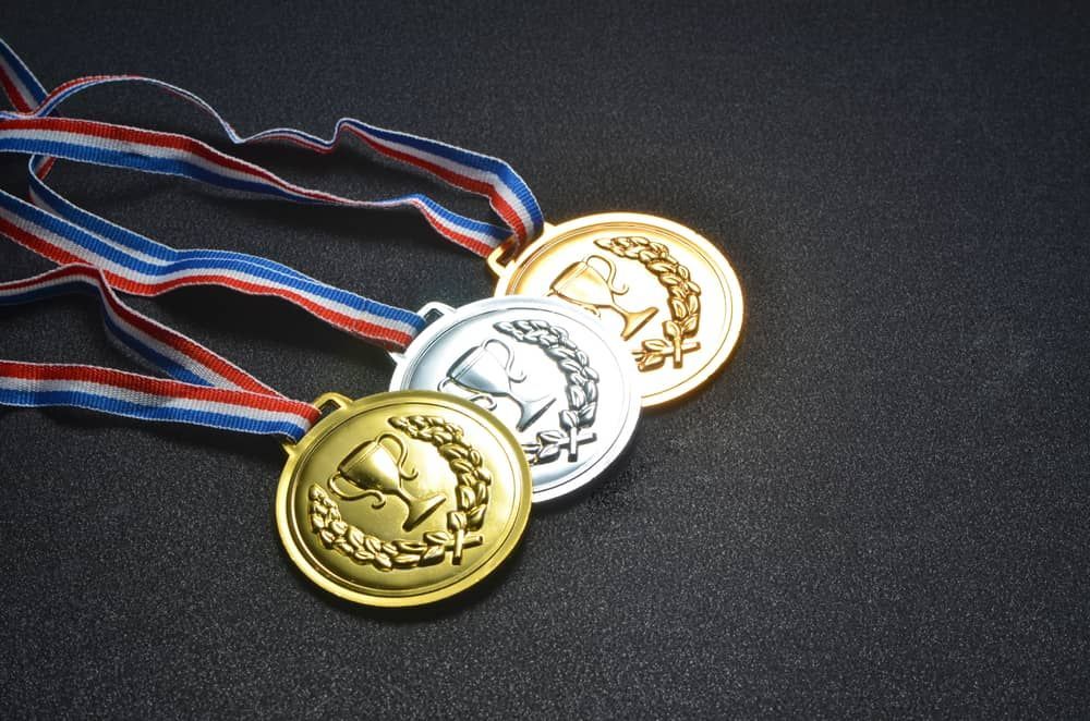 Three Gold Silver And Bronze Medals With Ribbons On A Black Surface — Accolades Awards Hunter Valley In Maitland, NSW