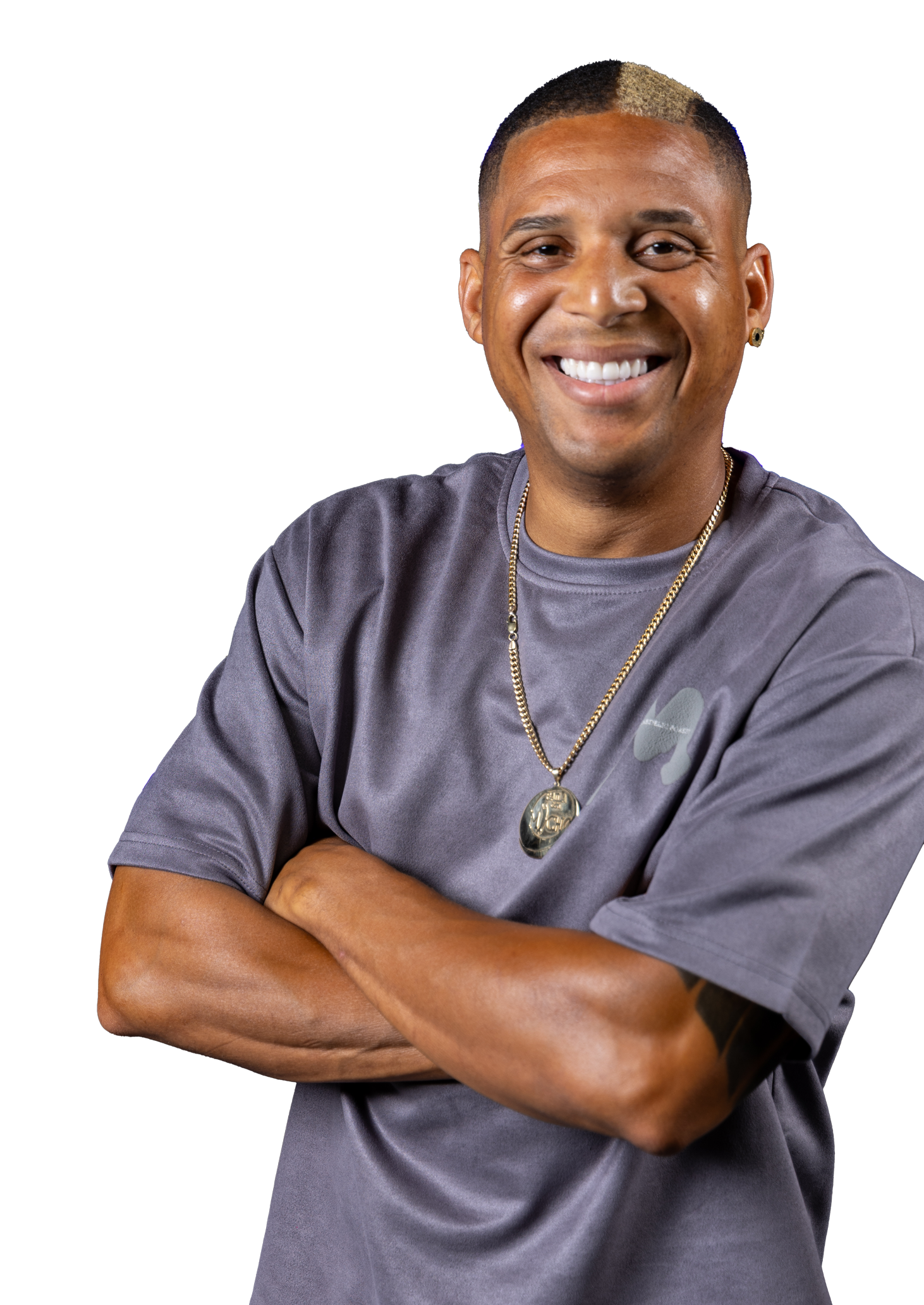 A man wearing a gray shirt and a gold necklace is smiling with his arms crossed.
