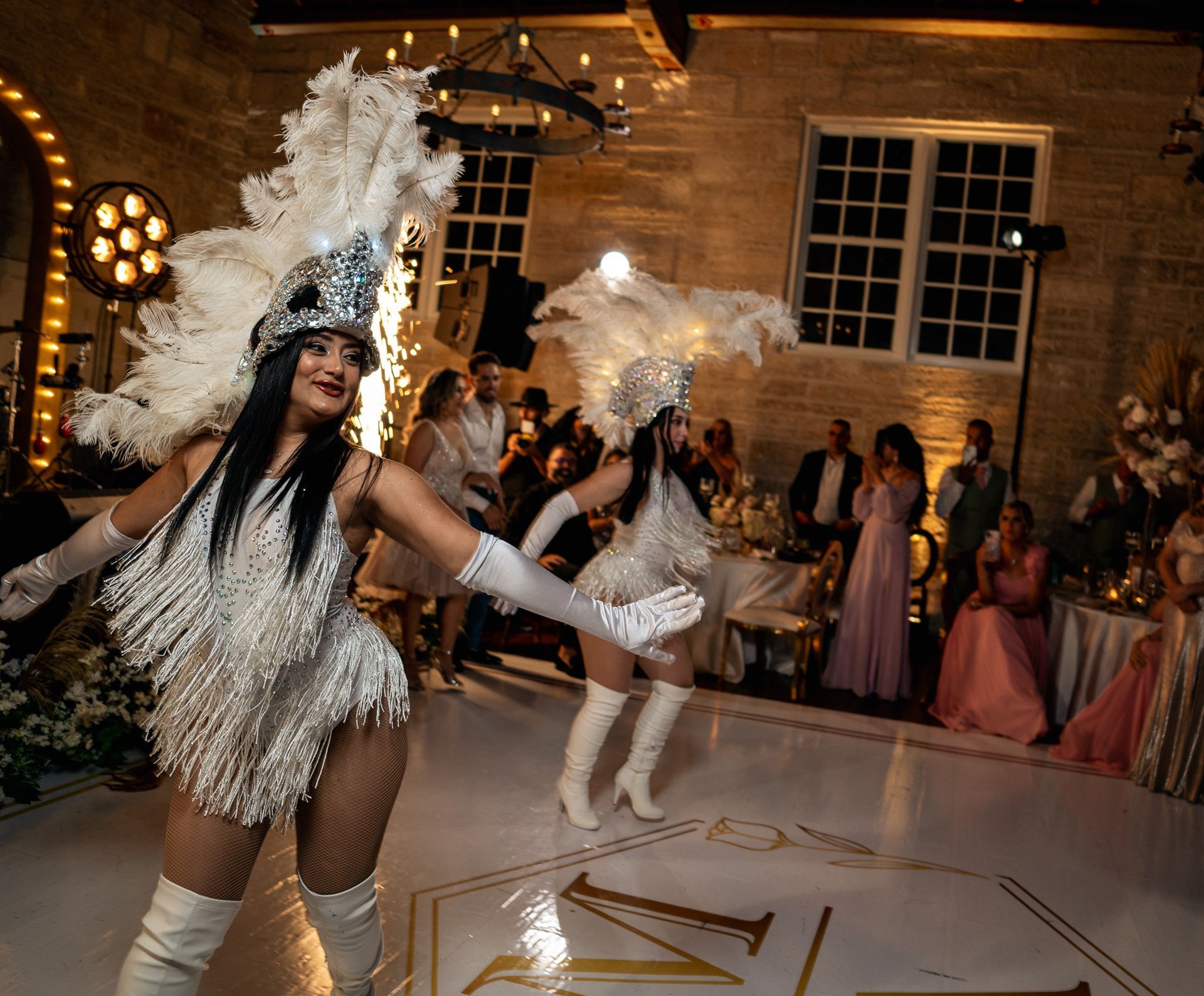 Two women in white feathered costumes are dancing on a dance floor.