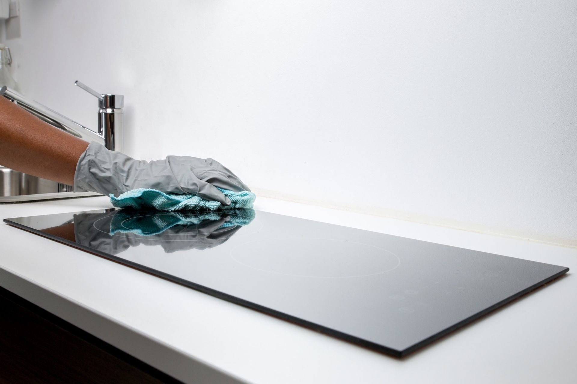 A person is cleaning a stove top with a cloth in a kitchen.