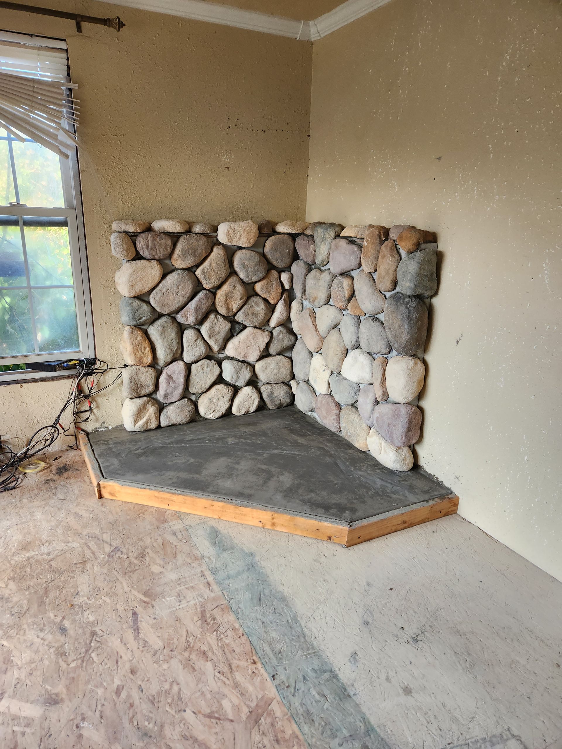 A stone fireplace is being built in the corner of a room.