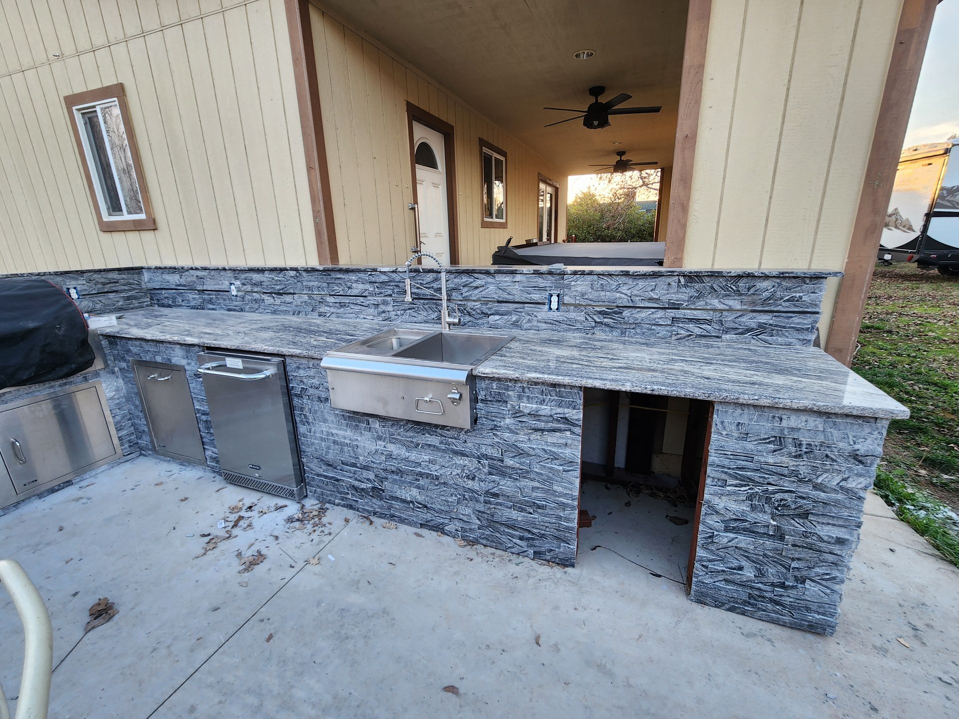 An outdoor kitchen with a sink , dishwasher , and grill.