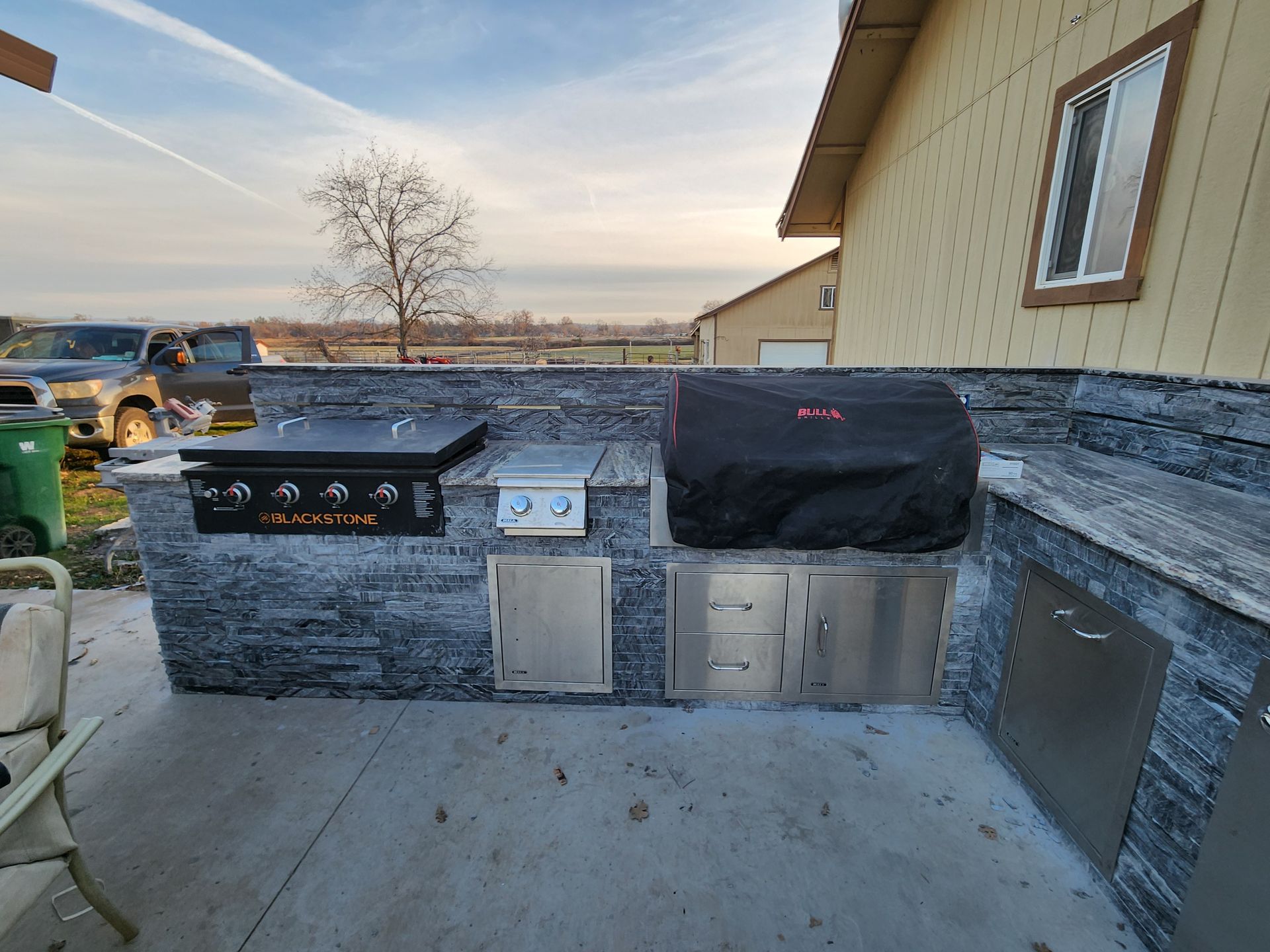 A stainless steel grill is sitting on a patio next to a house.