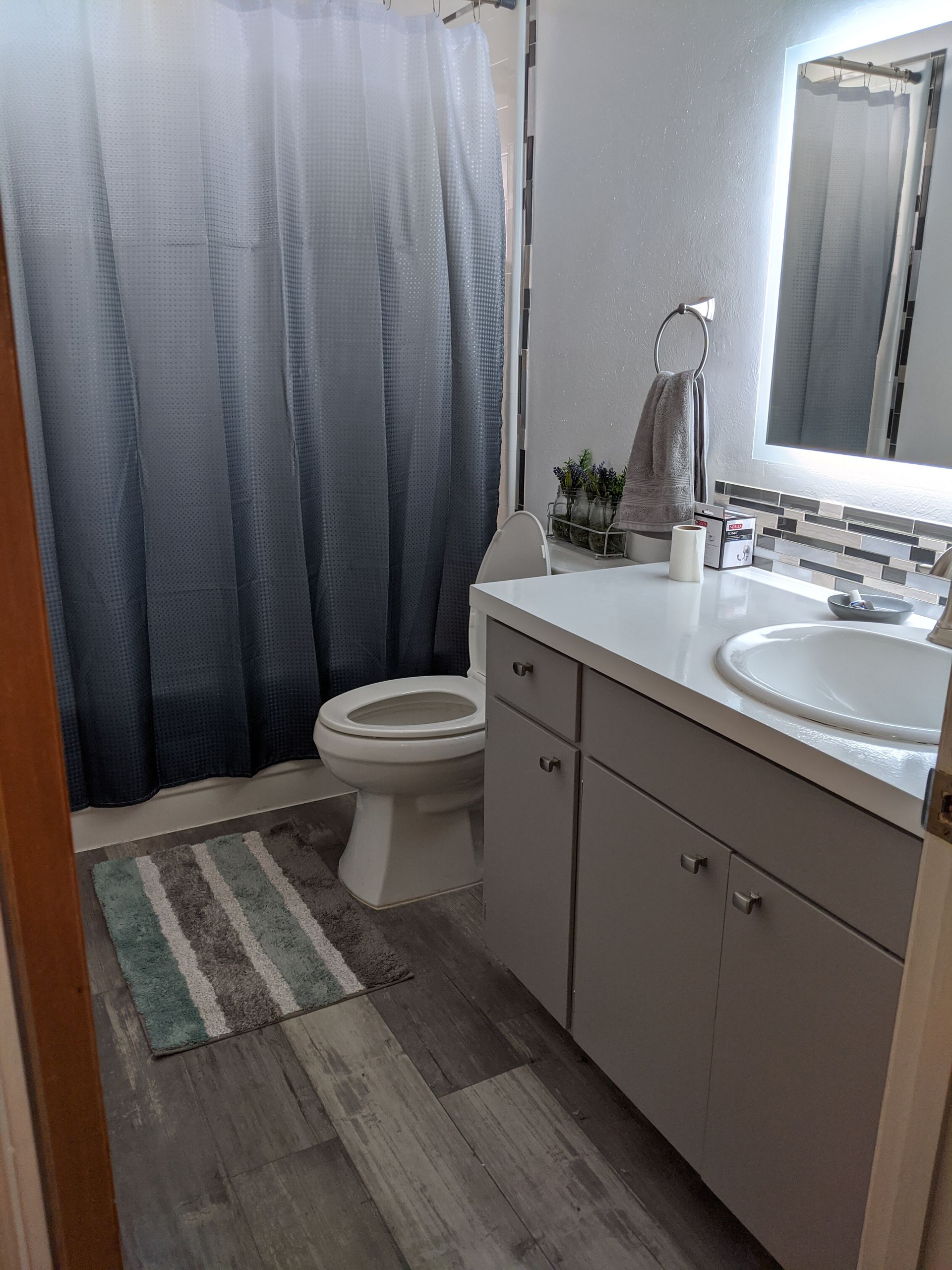 A bathroom with a toilet , sink , mirror and shower curtain.