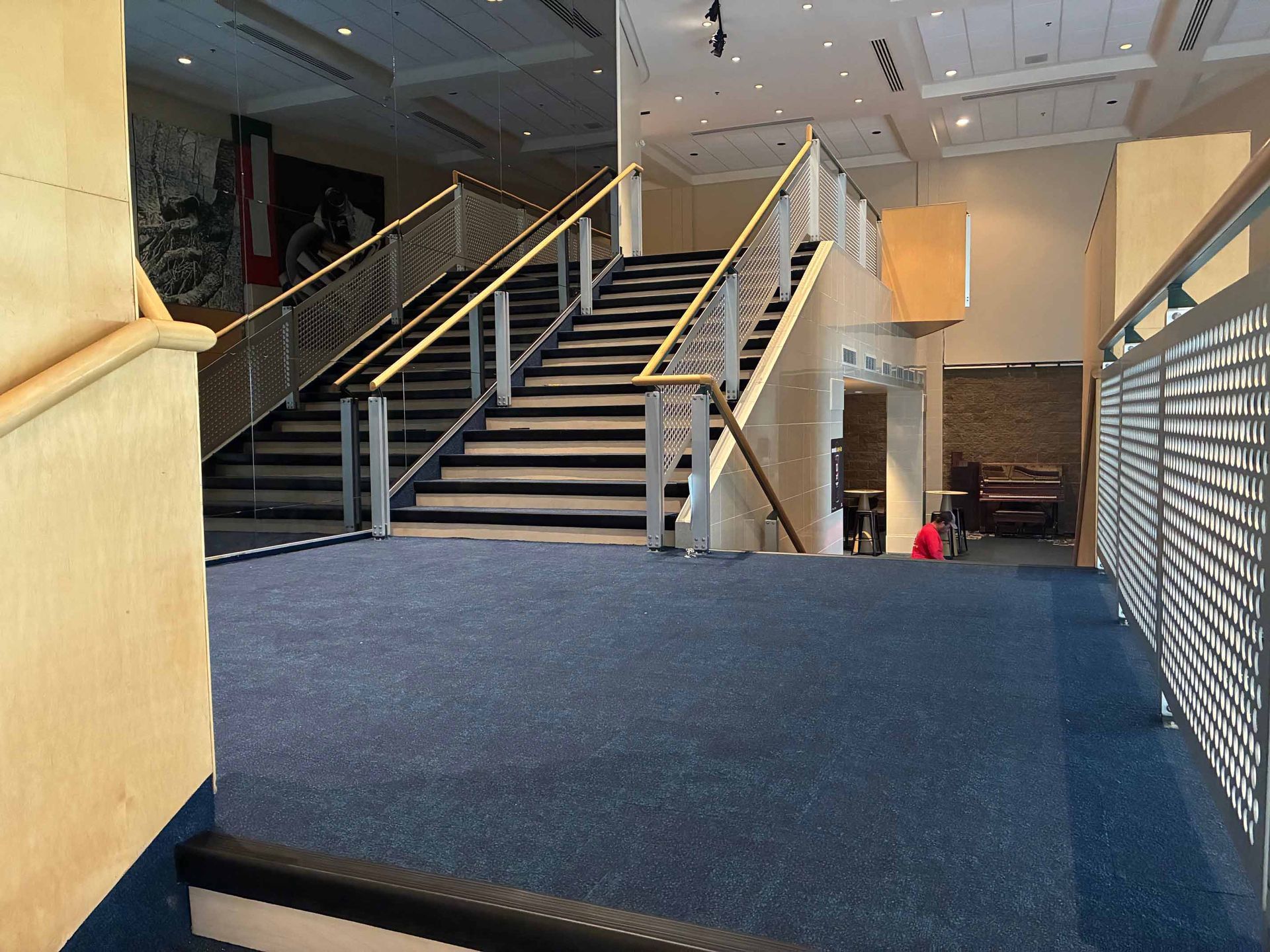 Vue intérieure d'un bâtiment avec escalier, rampes métalliques et moquette bleue.