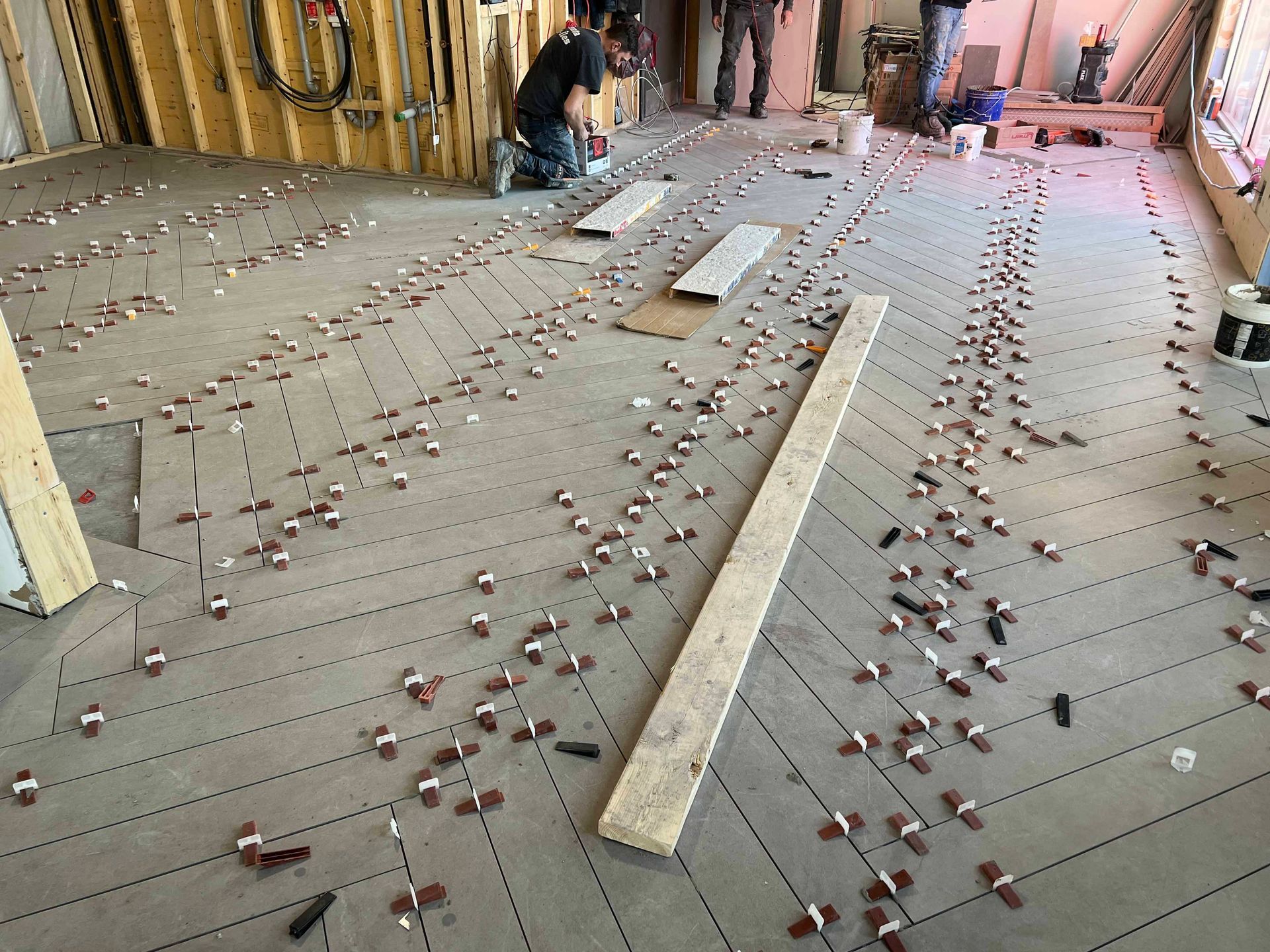 Chantier : sol recouvert de nombreux clips de nivellement, un ouvrier pose des carreaux.