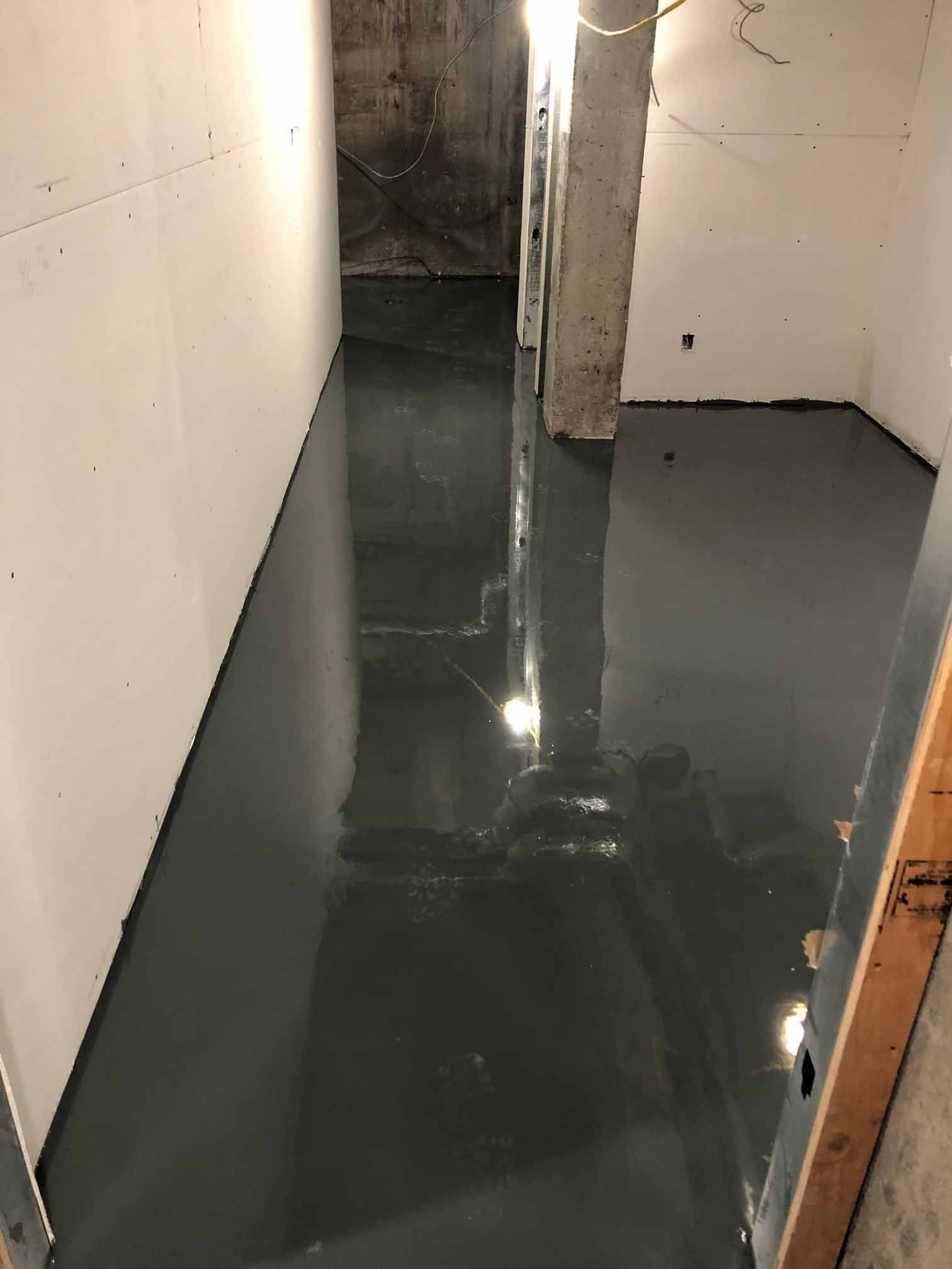 Sol en époxy gris foncé dans une pièce du sous-sol, reflétant les murs et les colonnes de soutien.