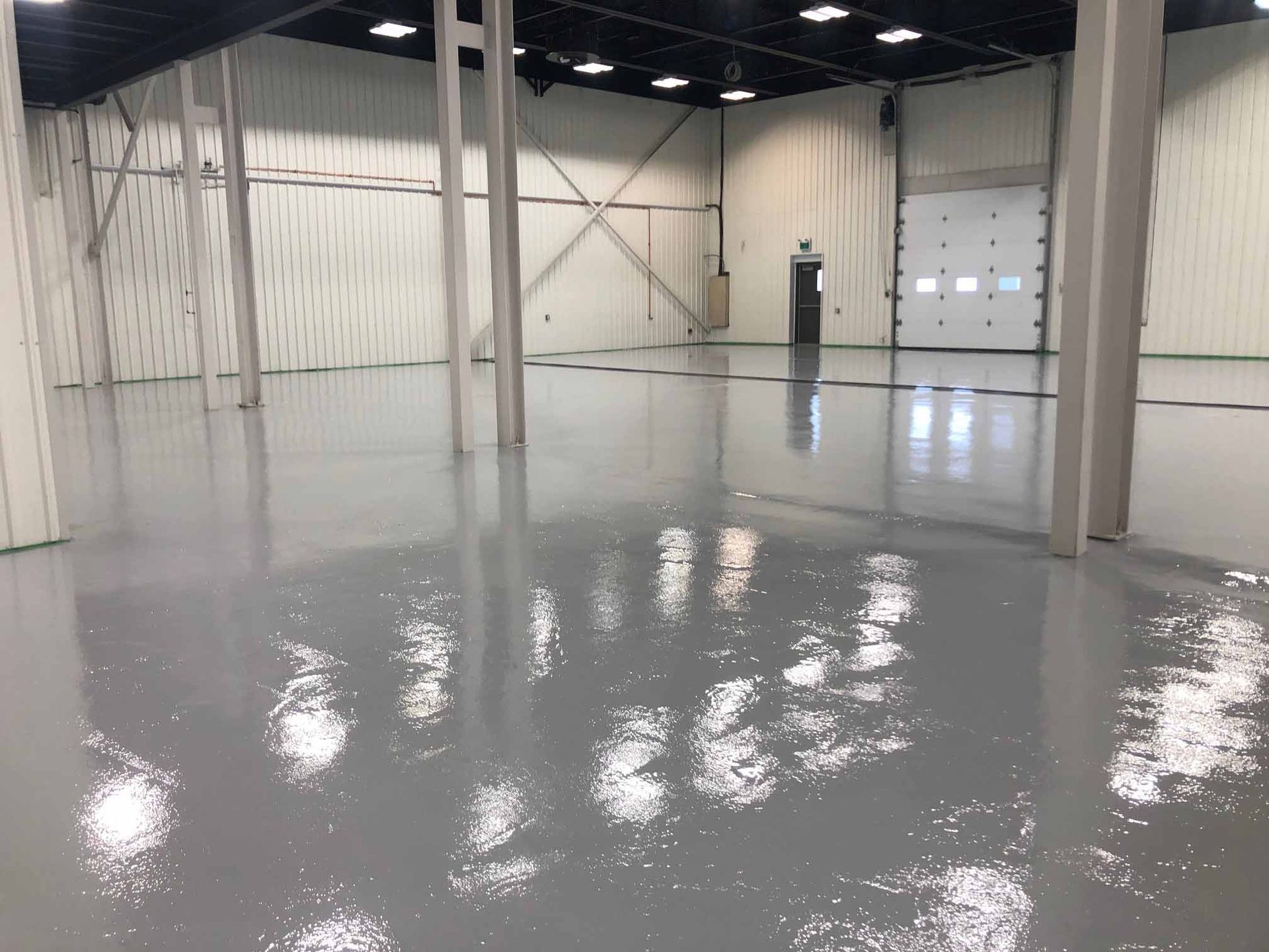 Un vaste espace industriel vide, avec un sol gris brillant et un éclairage zénithal intense.