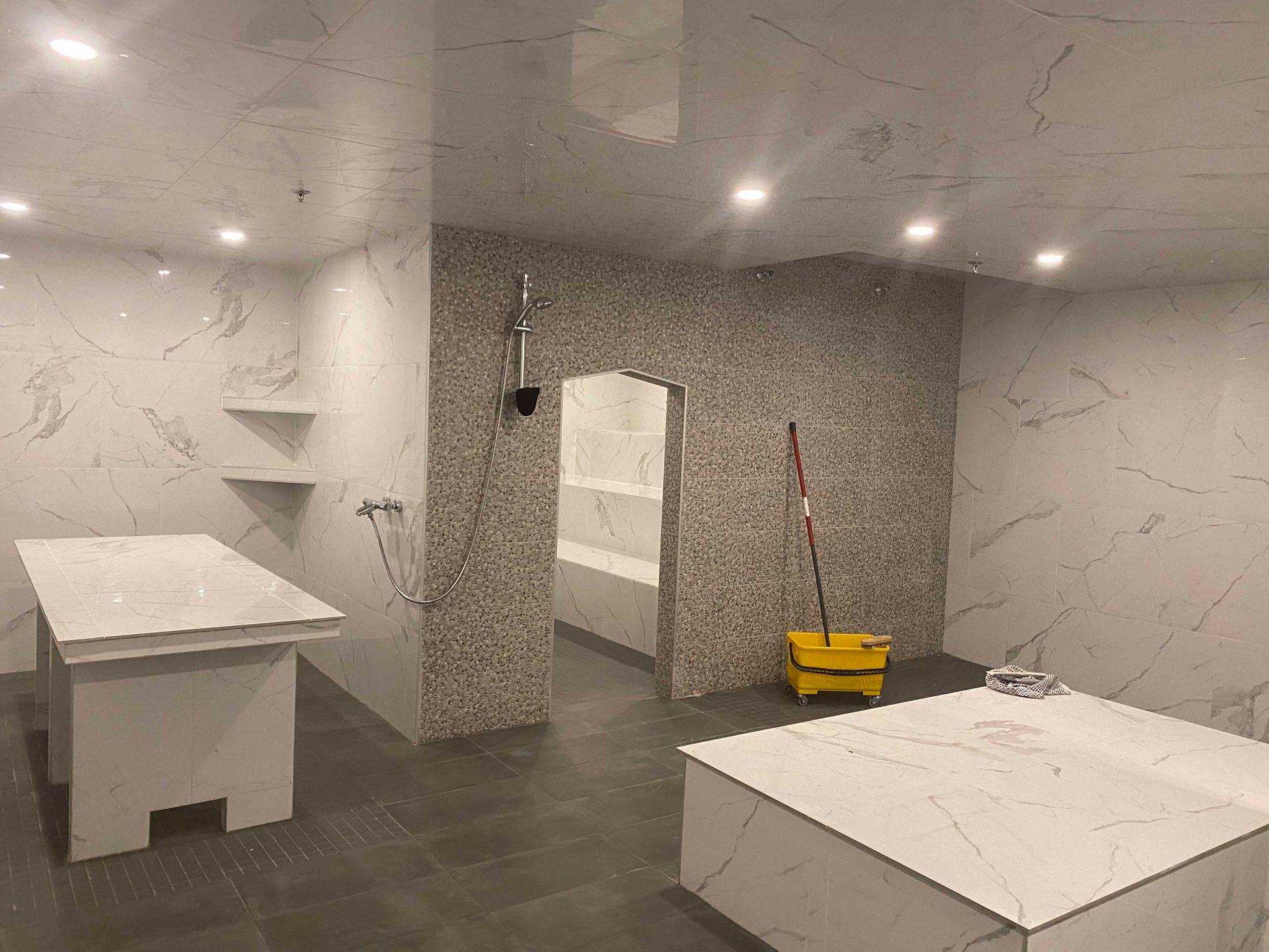 Spacieuse salle de spa avec murs et comptoirs carrelés façon marbre, une douche et une petite alcôve carrelée de mosaïque.
