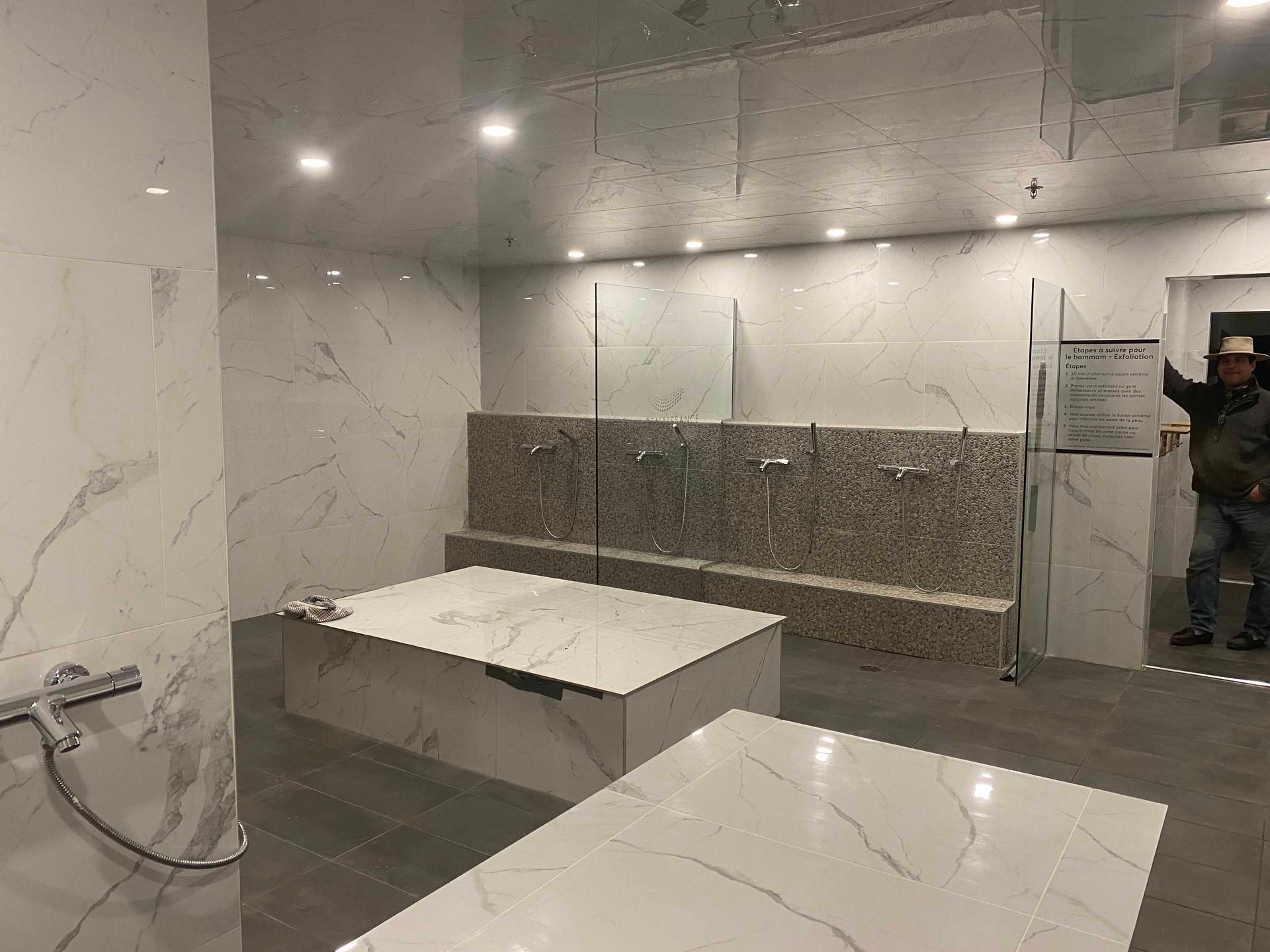 Salle de bains avec murs et comptoirs en marbre ; personne debout, tenant un outil de mesure.