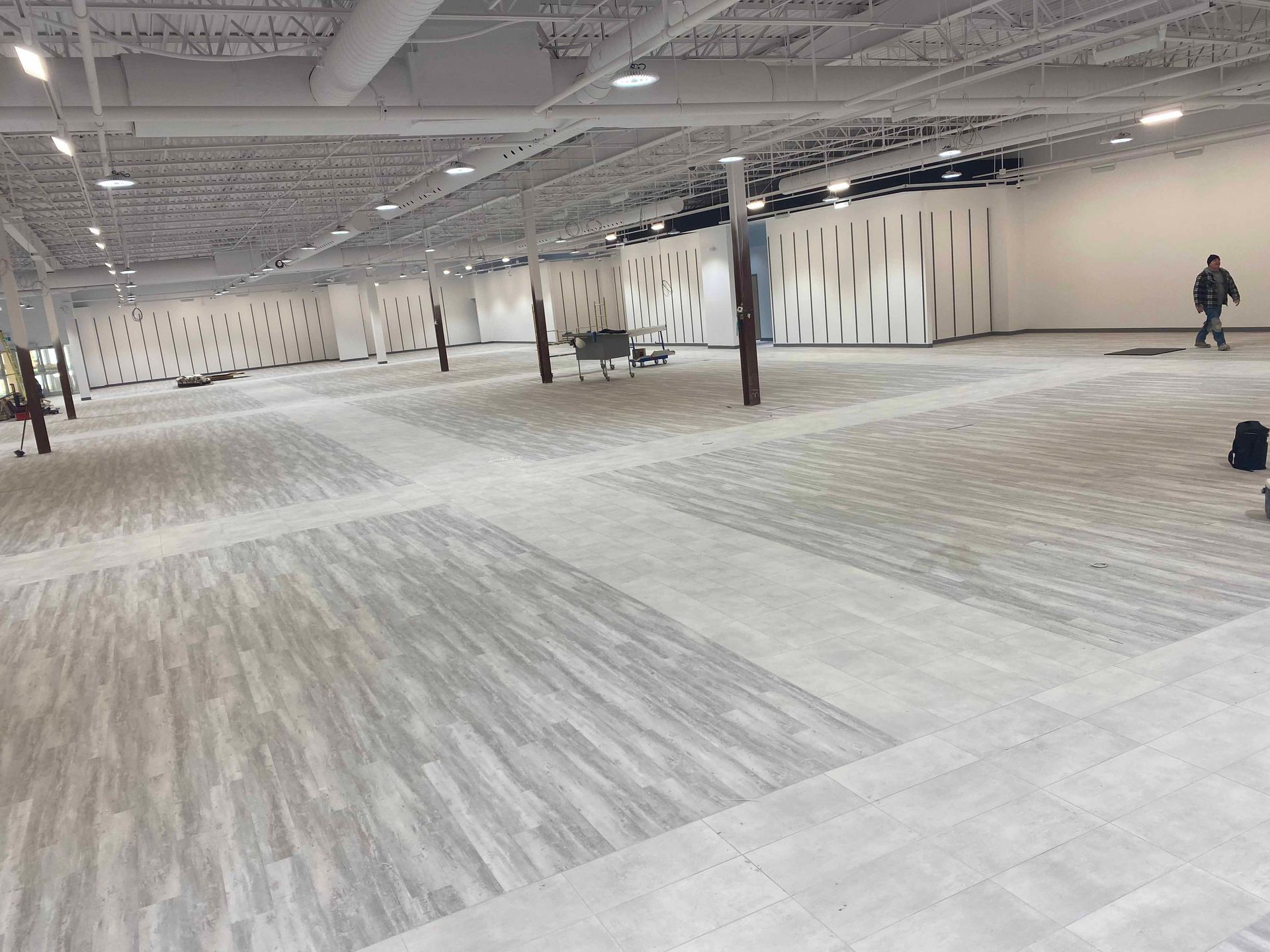 Grand espace intérieur ouvert avec un sol gris à motifs et des murs bruts ; une personne qui marche.