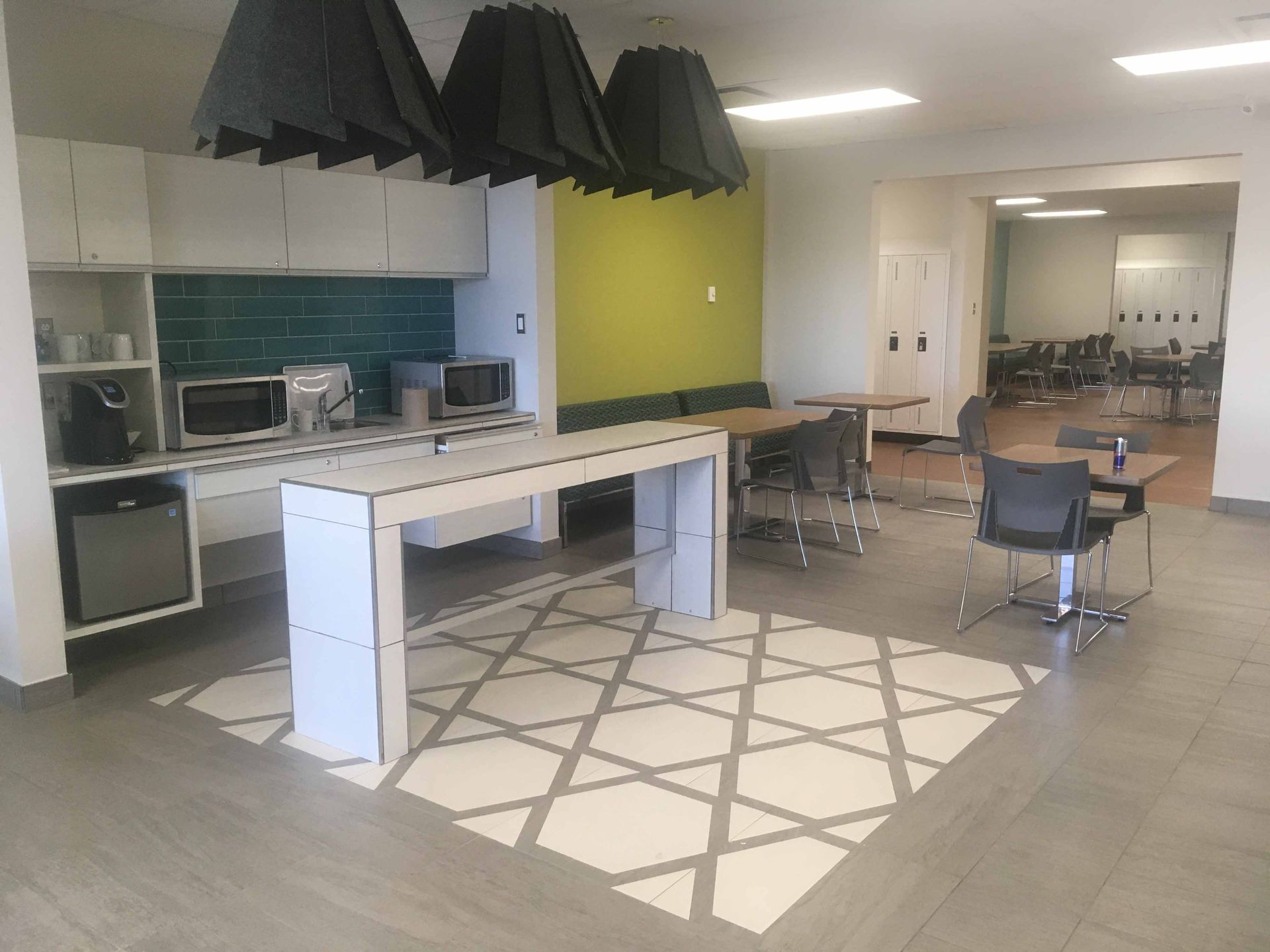 Cuisine de bureau moderne avec armoires blanches, crédence turquoise et carrelage gris et blanc au sol.