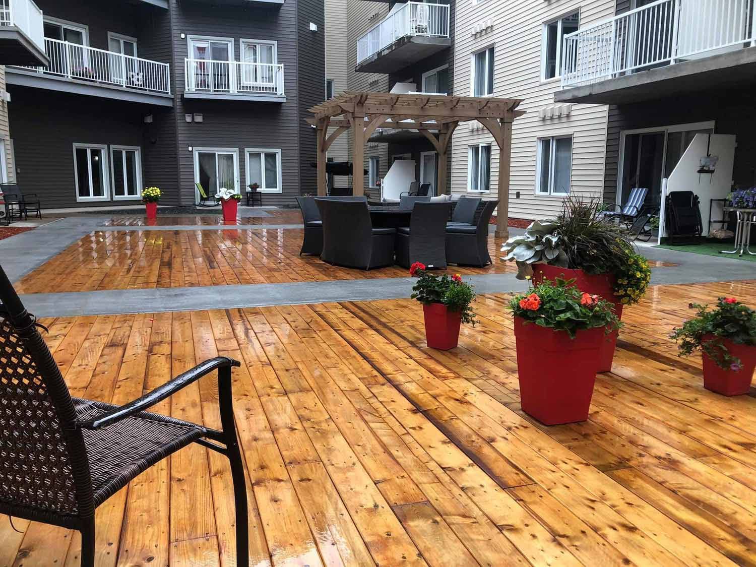 Cour intérieure avec terrasse en bois, mobilier de jardin, pots de fleurs rouges et immeuble d'appartements en arrière-plan.