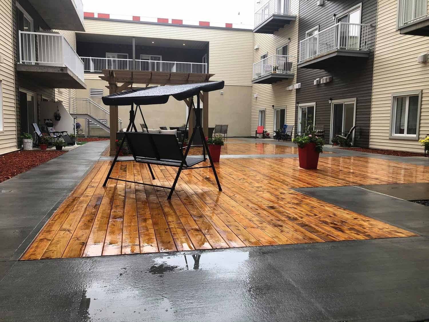 Cour intérieure avec terrasse en bois, balançoire et immeubles d'appartements environnants ; surface humide.