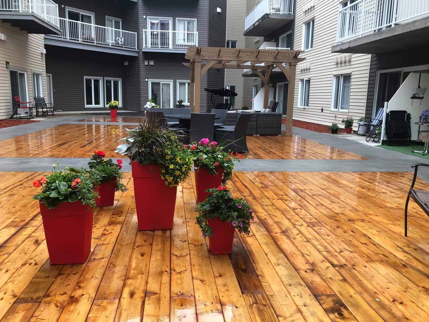 Cour extérieure avec terrasse en bois, jardinières rouges et coin salon.