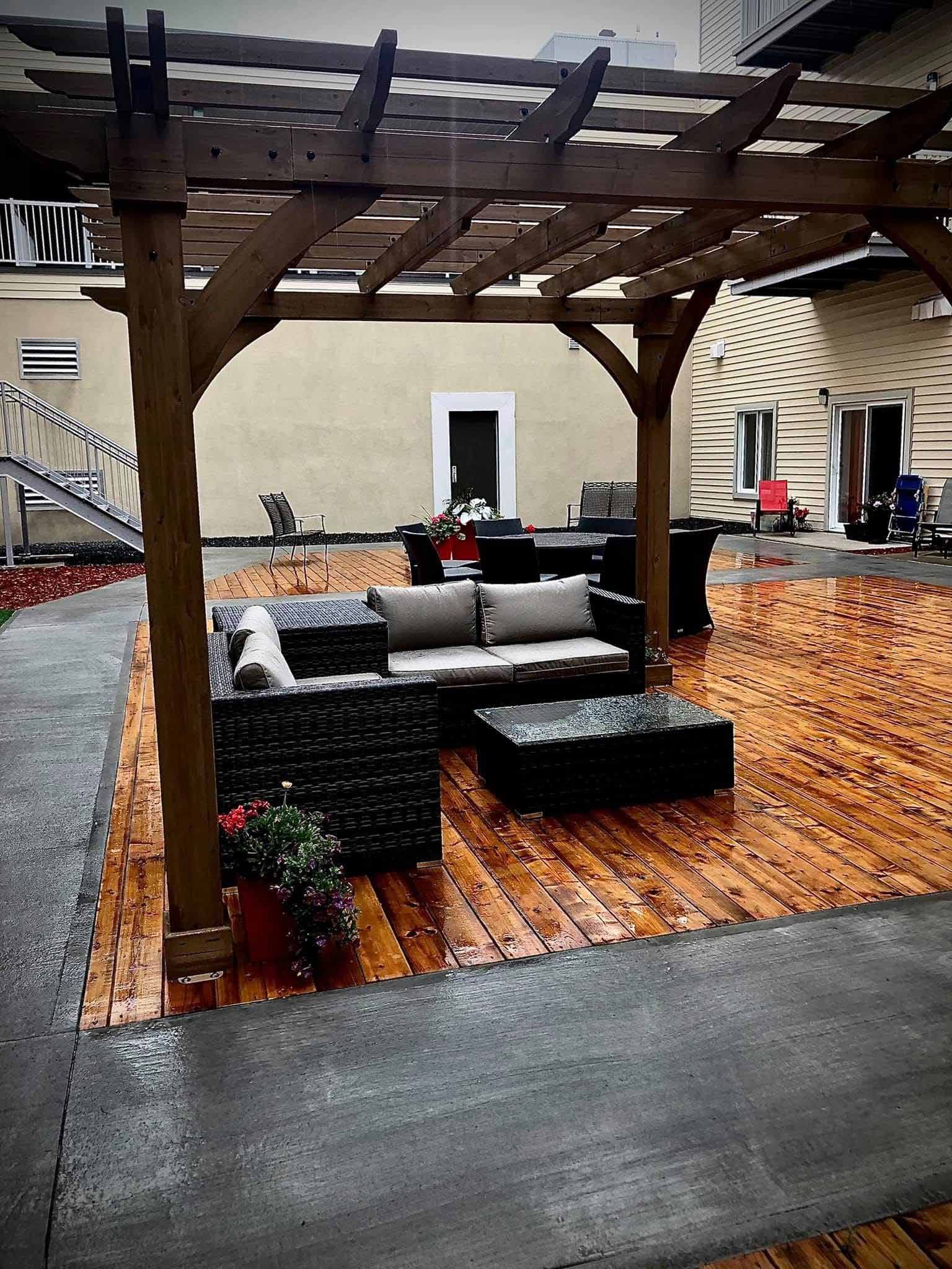 Pergola en bois surplombant un coin salon extérieur avec mobilier en osier foncé et terrasse en bois.