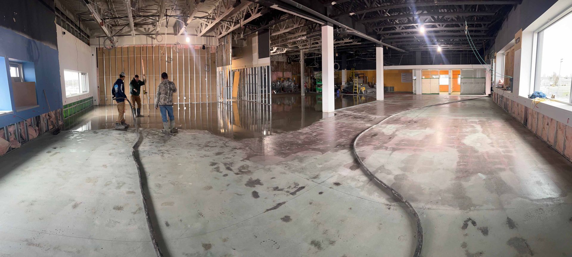 Vue intérieure d'un bâtiment inondé, avec des ouvriers qui y circulent. On aperçoit la structure à nu, de l'eau et des débris.