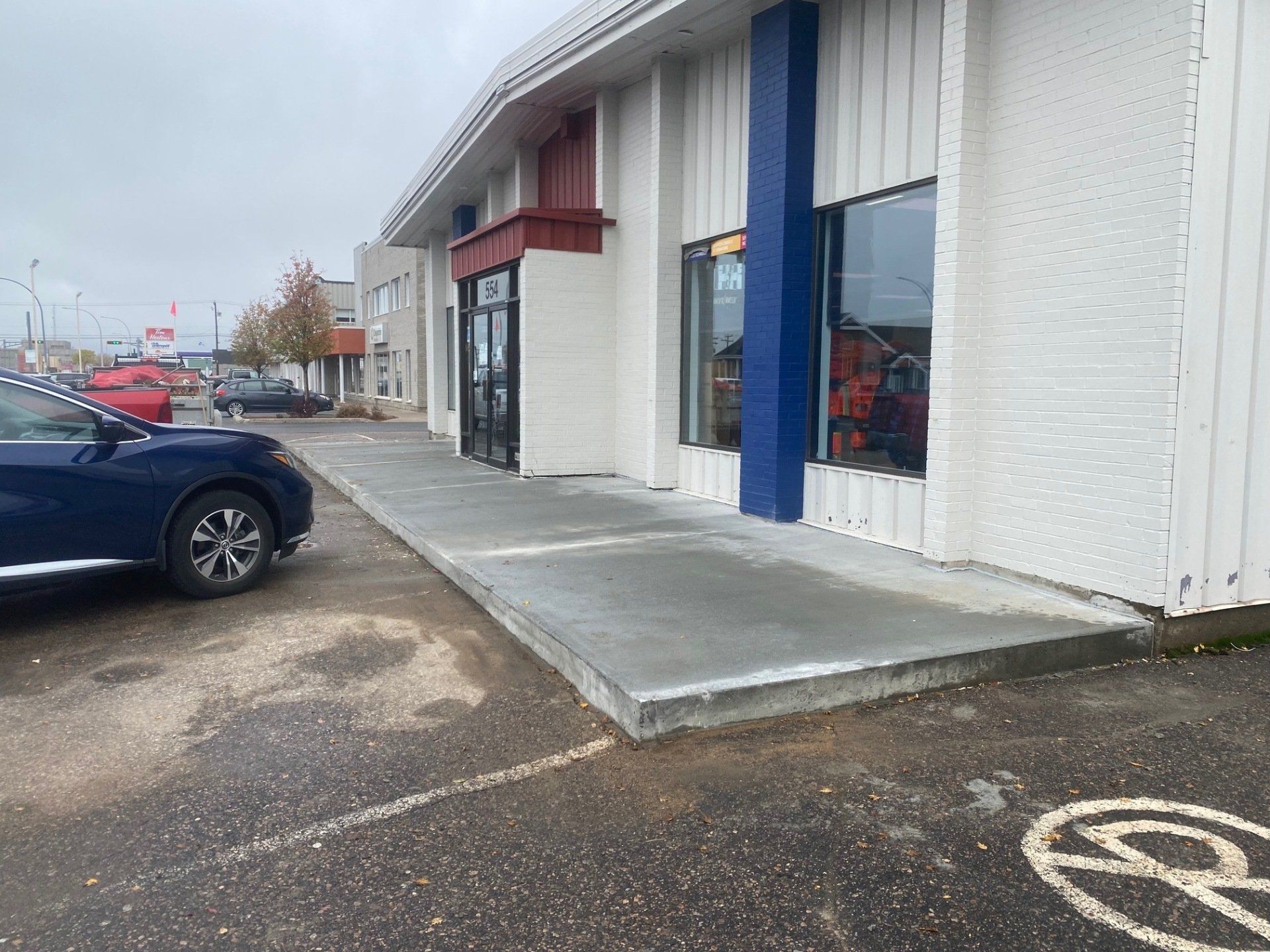 Extérieur d'un bâtiment avec une rampe en béton et des touches de bleu. Une voiture bleue est garée au premier plan.
