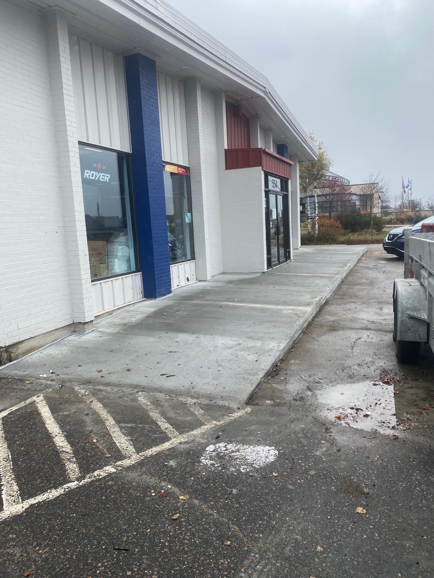 Vue extérieure d'un bâtiment avec une rampe en béton et un parking par temps nuageux.