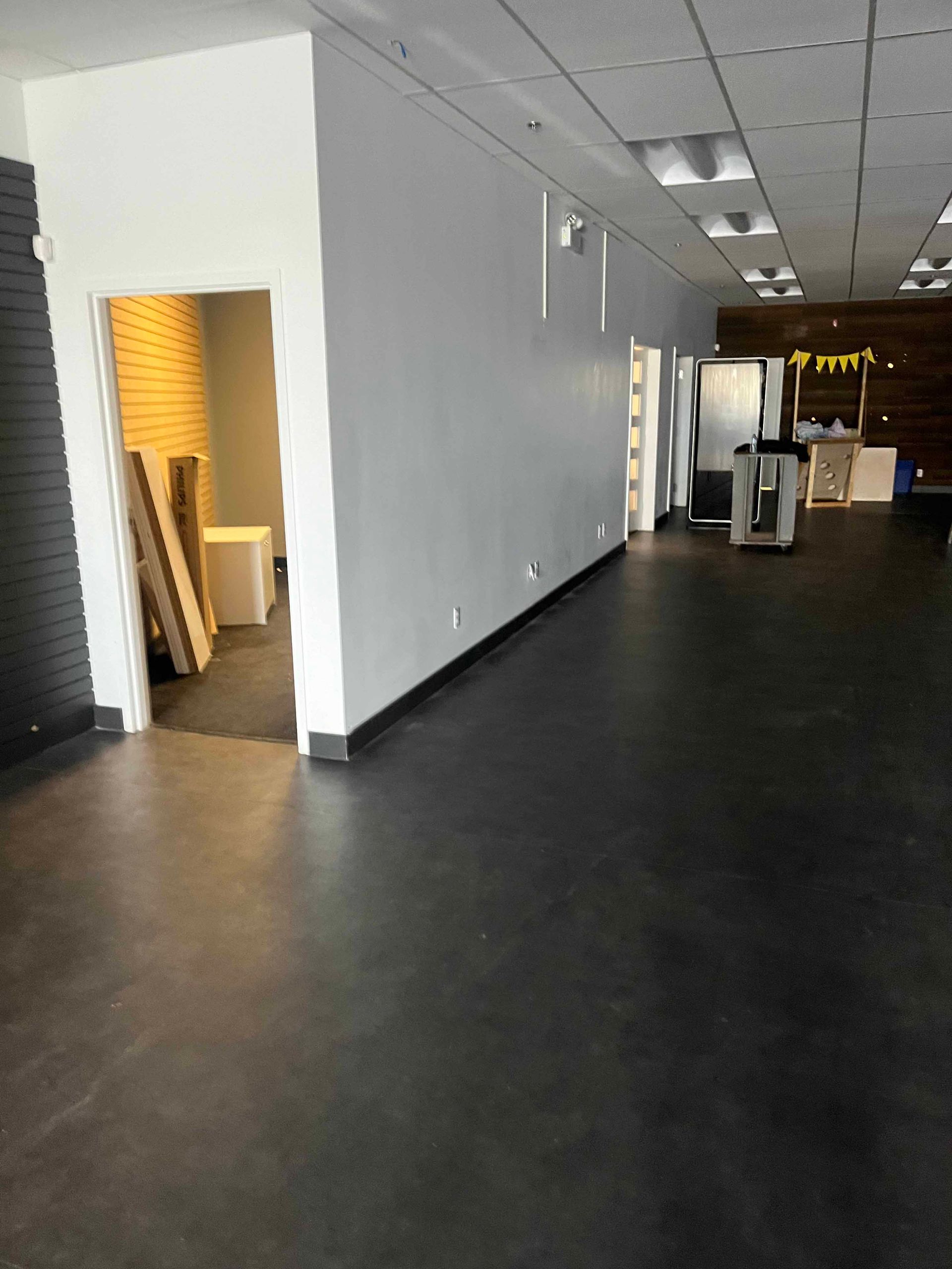Intérieur commercial vide avec sol sombre, murs blancs et portes ouvertes.