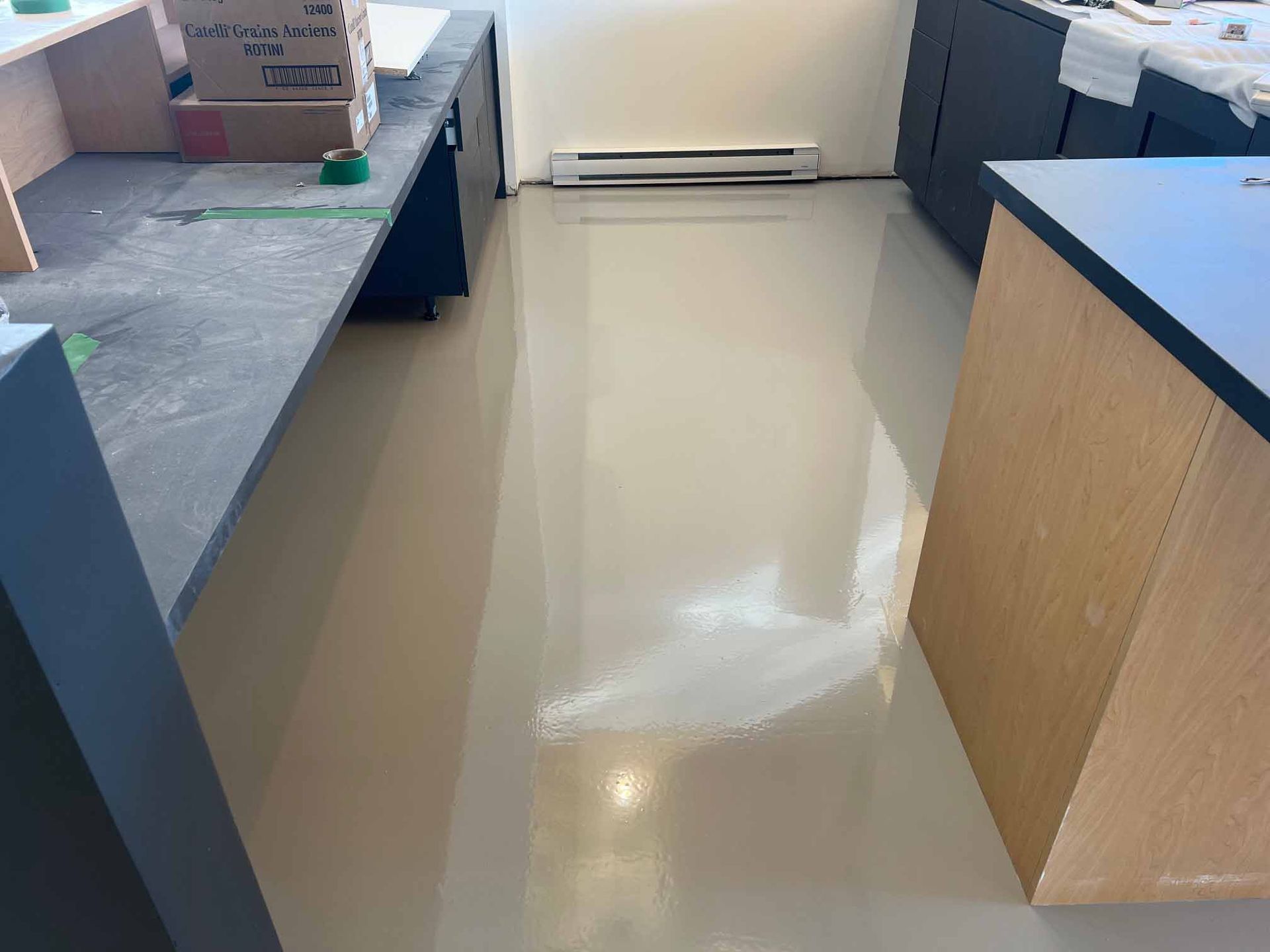 Sol en résine époxy beige dans une pièce aux meubles gris et en bois. Un radiateur est fixé au mur blanc.