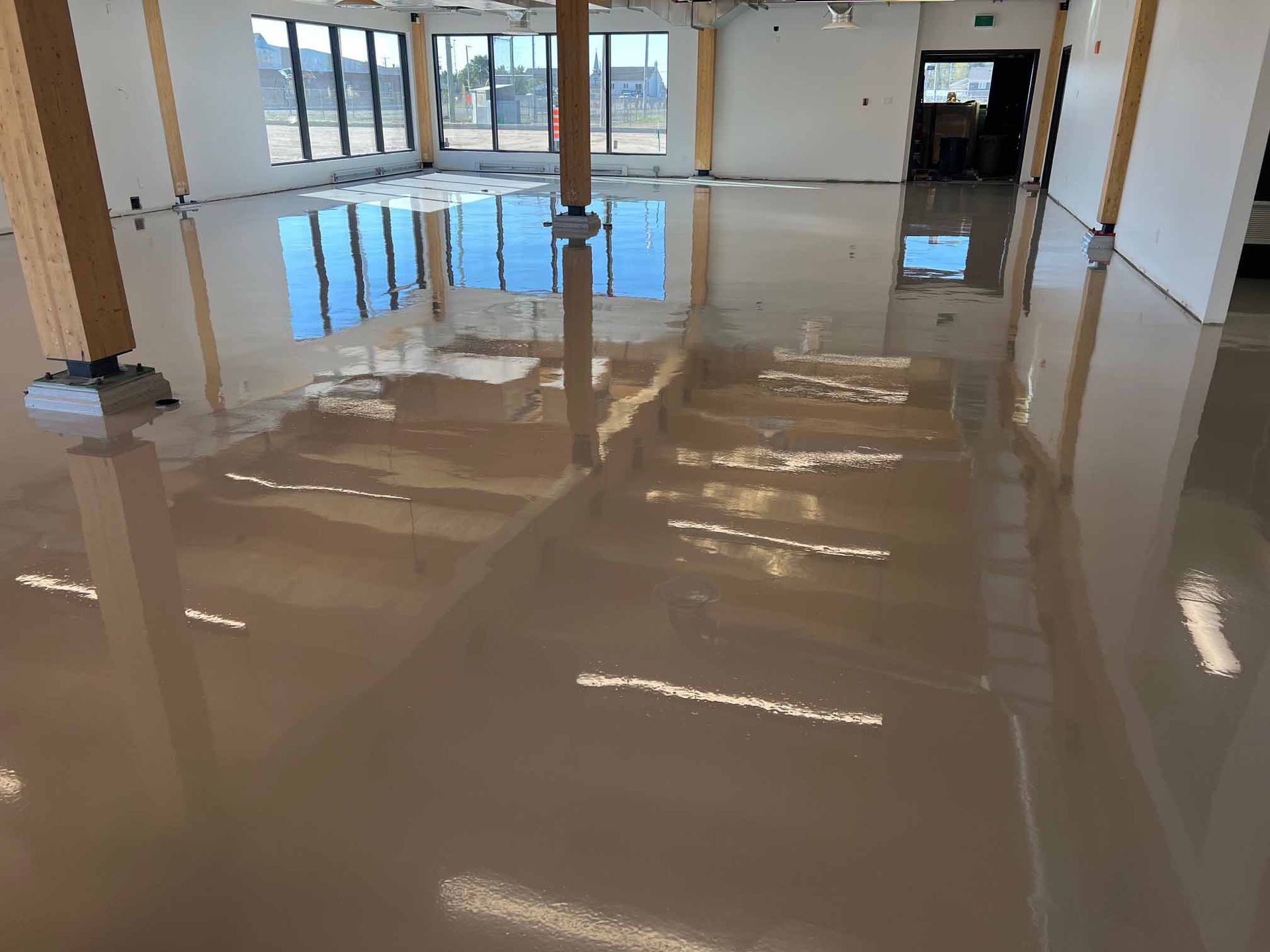 Vue intérieure d'un bâtiment dont le sol, d'un beige brillant et fraîchement coulé, reflète le ciel et la structure intérieure.