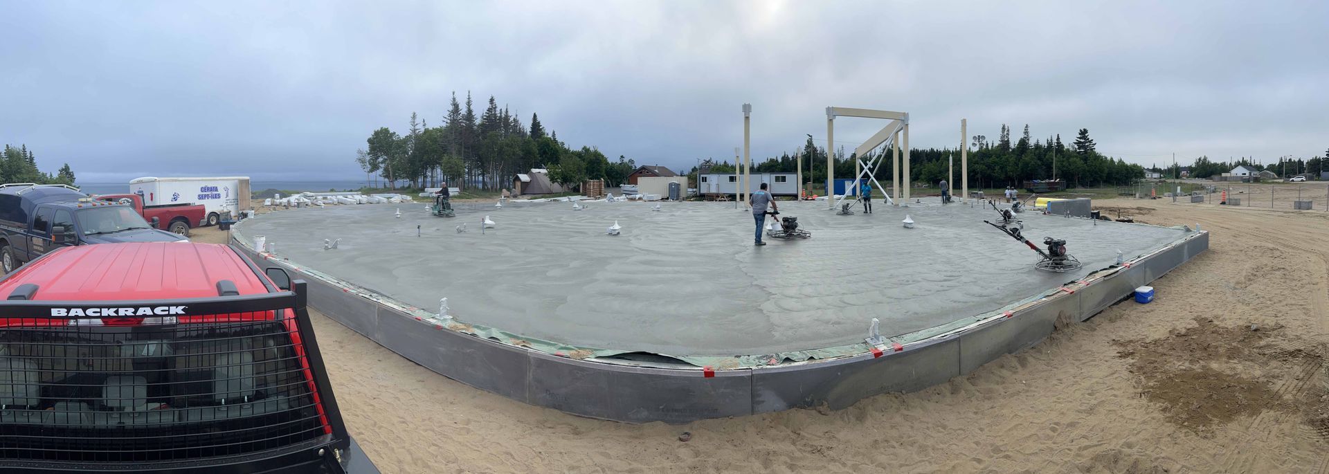 Une grande dalle de béton grise entourée d'une barrière noire, avec des engins de chantier et des arbres en arrière-plan.