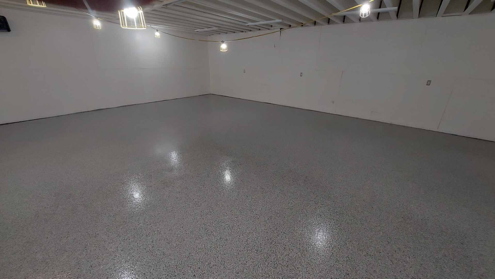 Pièce vide avec un sol en époxy gris moucheté et des murs blancs, éclairée par des spots encastrés au plafond.